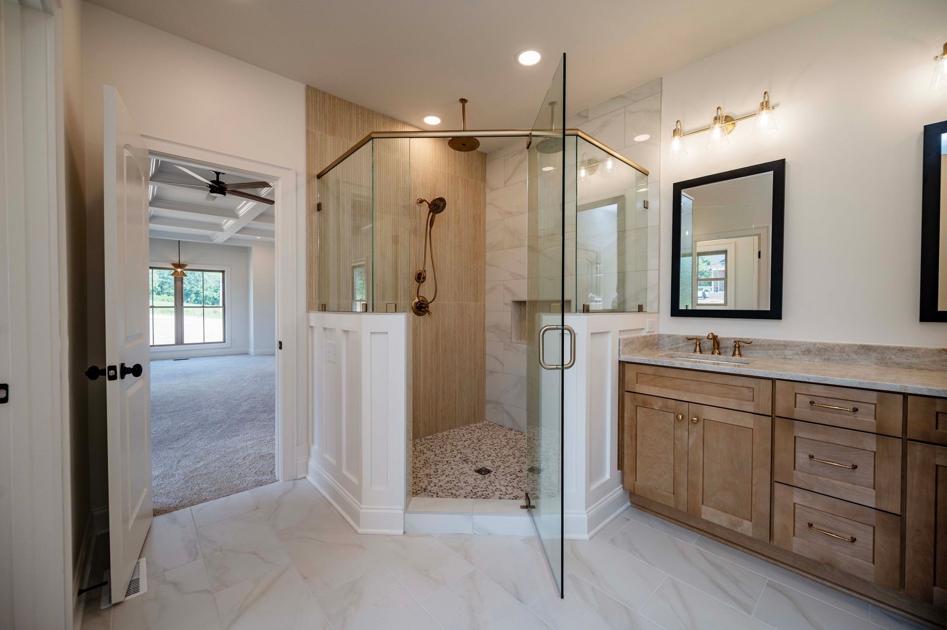 Bathroom with walk-in shower, vanity, and open doorway to bedroom with neutral colors and modern design.