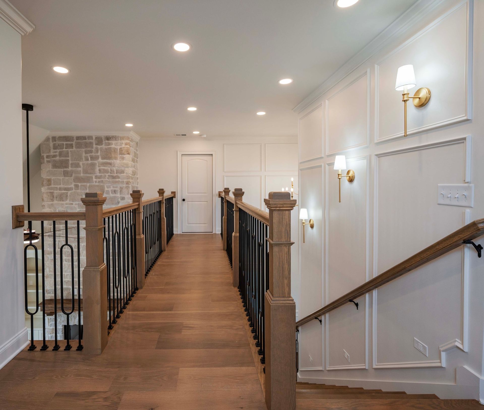 Hallway with wooden floor, stairs, white walls, and decorative paneling.