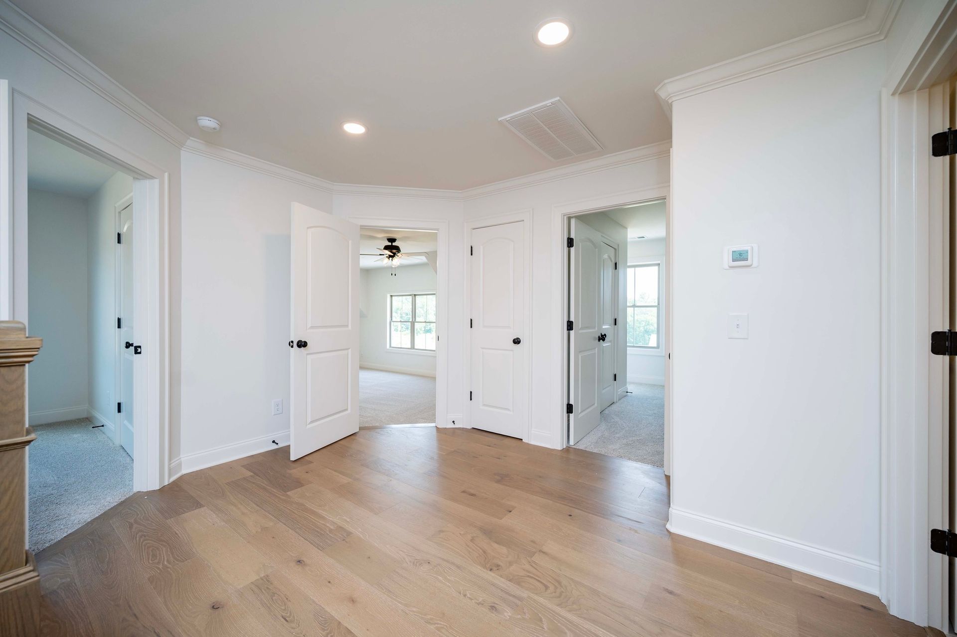 Hallway with light wood floors, white walls, and multiple doors leading to other rooms.