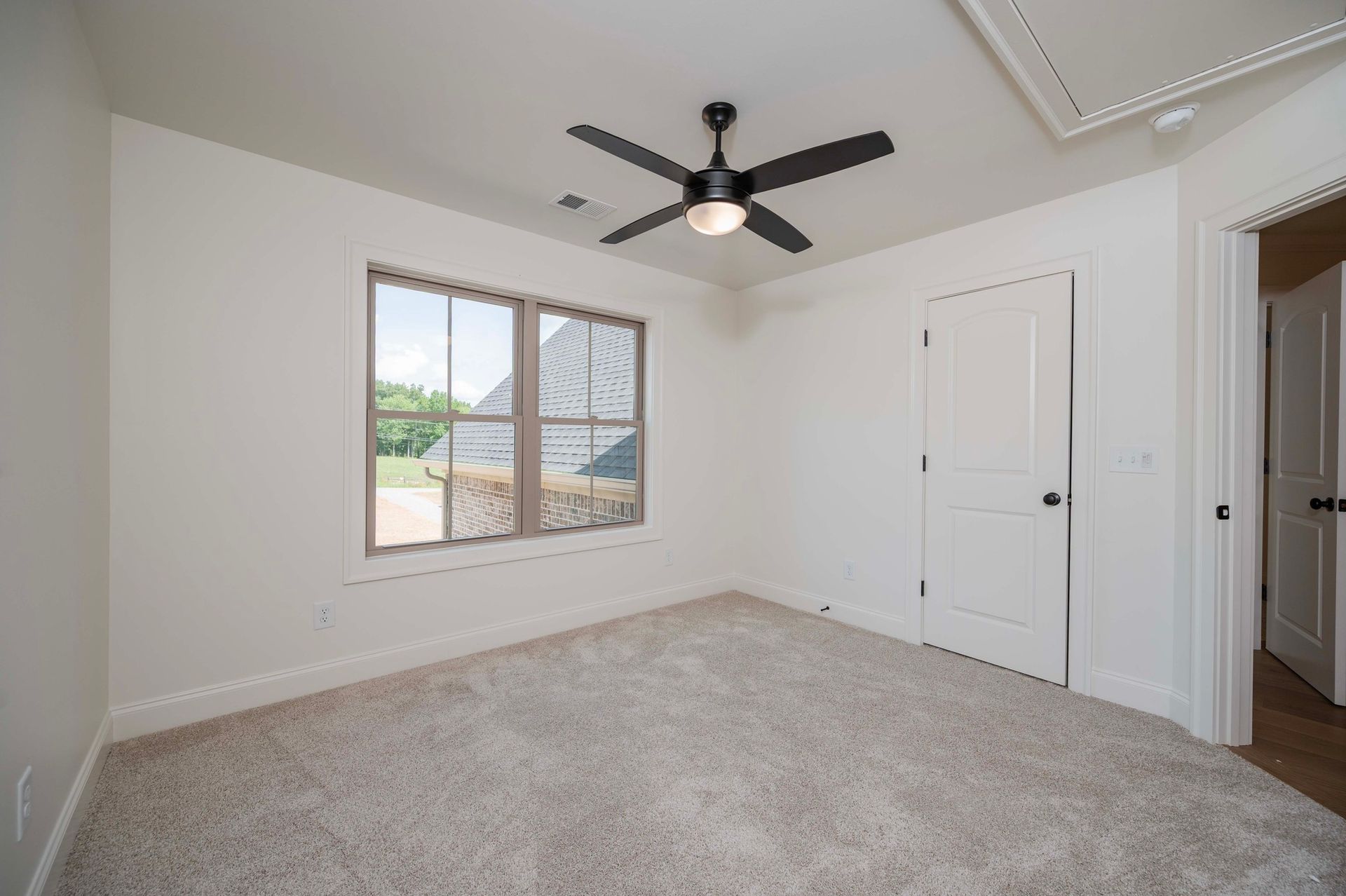 Empty bedroom with neutral carpet, white walls, ceiling fan, and window.