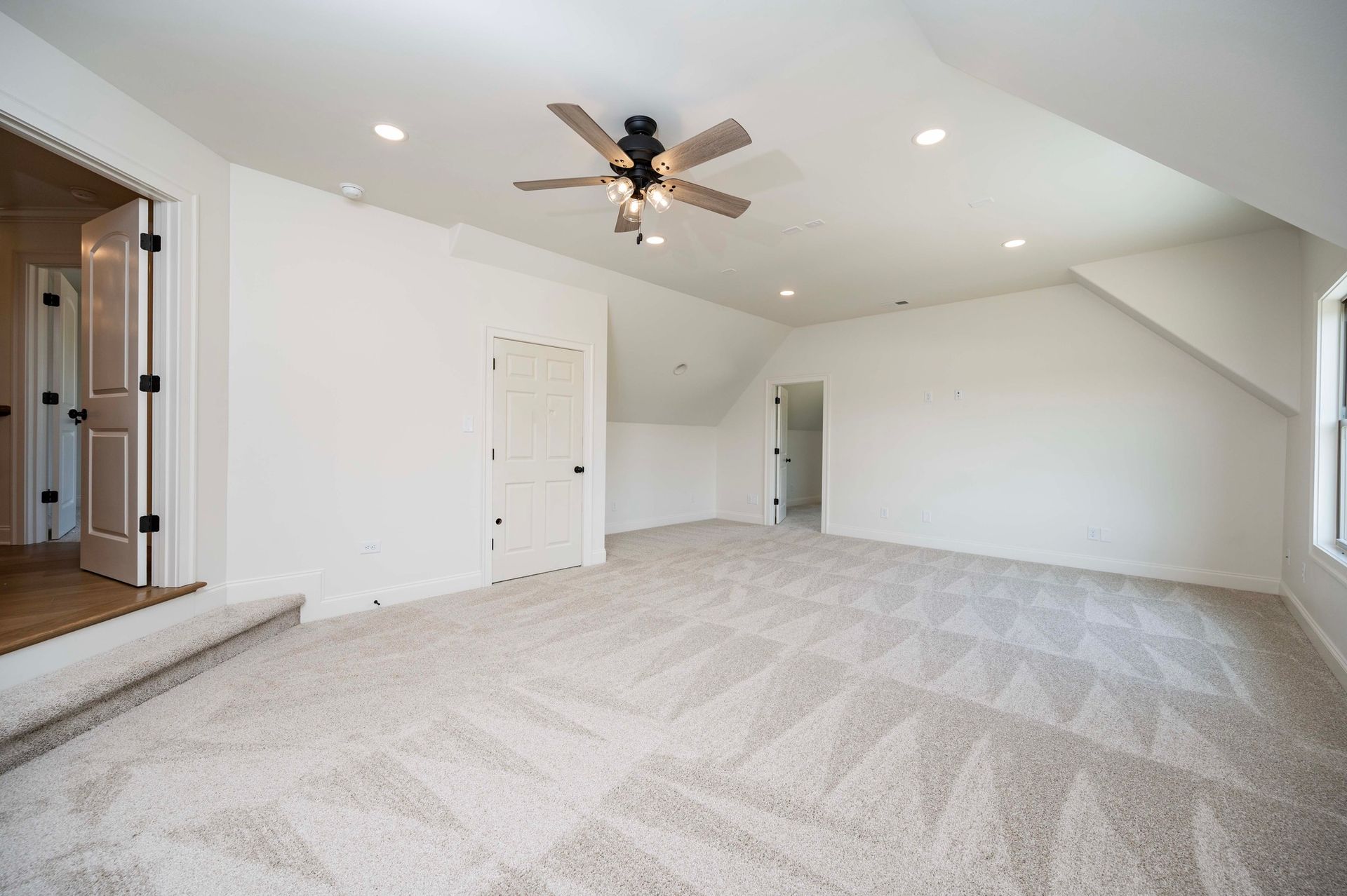 Empty room with beige carpet, white walls, and a ceiling fan. Doorways lead to other rooms.