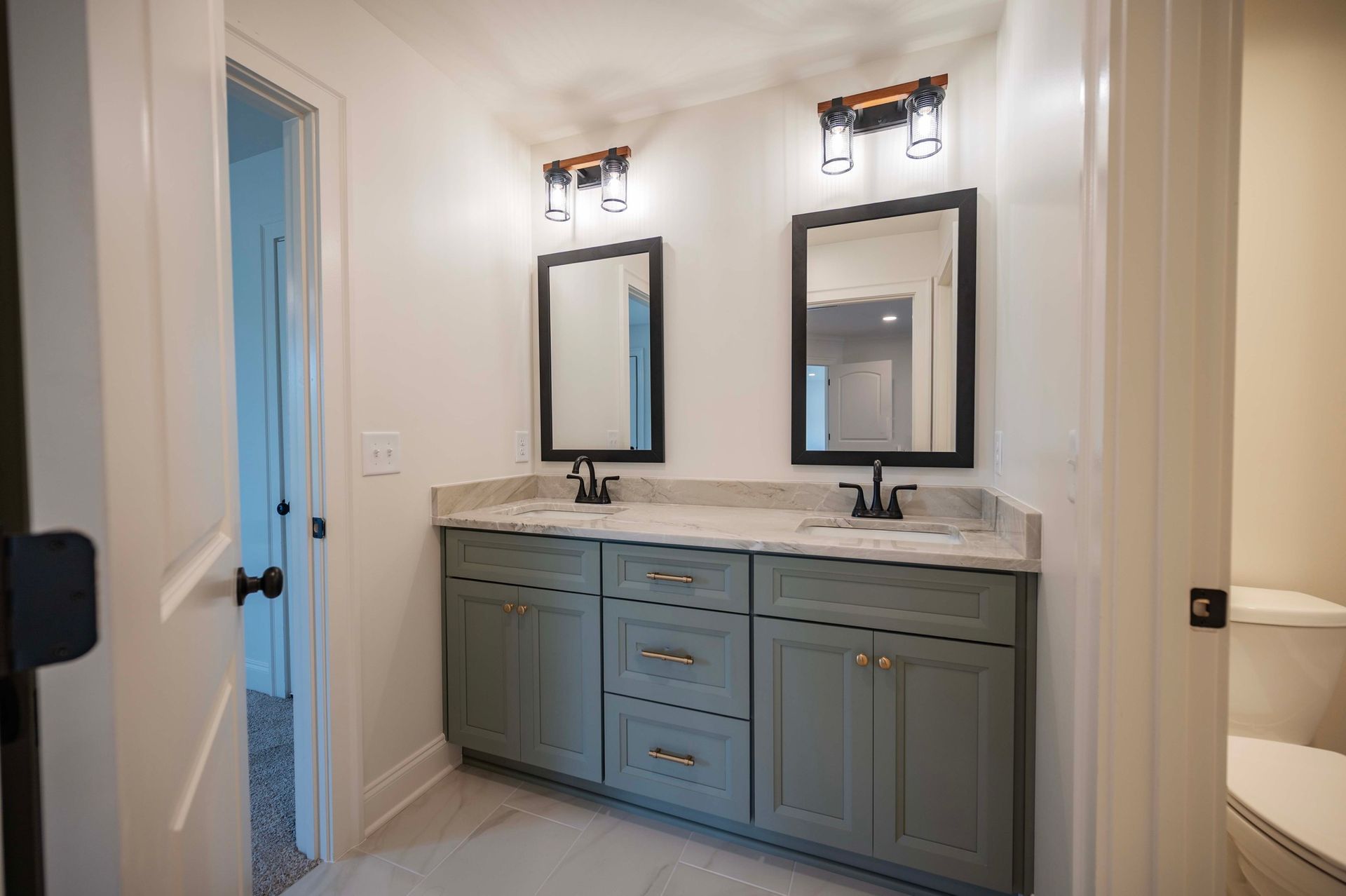 Bathroom with double vanity, green cabinets, two black-framed mirrors, and white countertops.