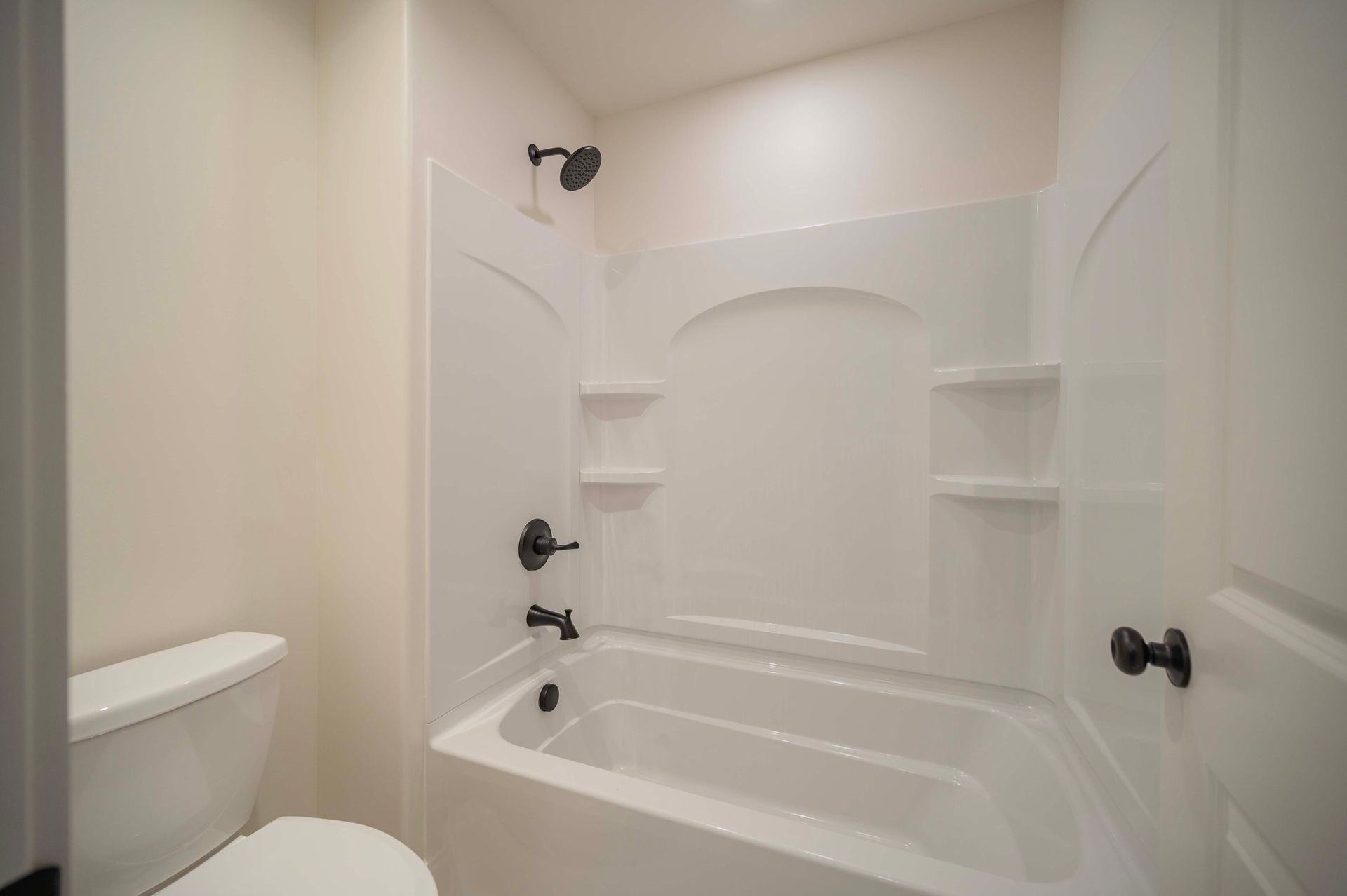 White bathroom with a tub, toilet, and black fixtures.