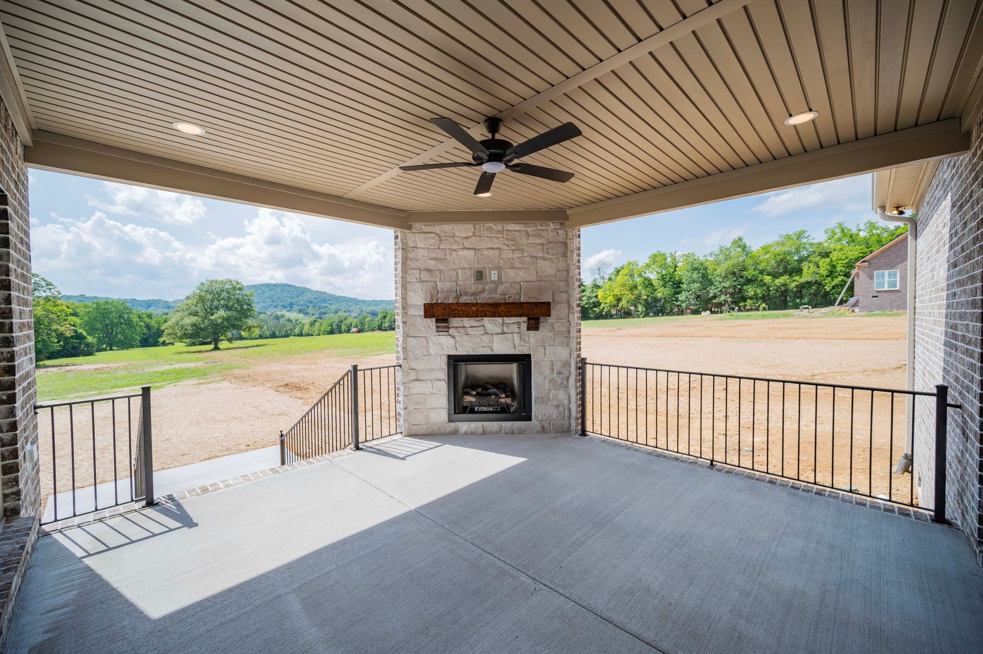 Covered patio with fireplace overlooking a grassy field and distant hills.