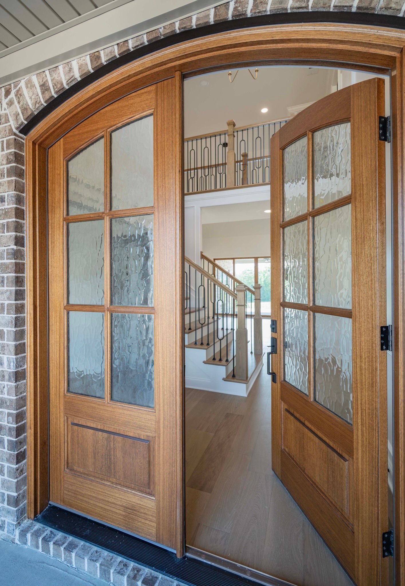 Wooden double doors open into a home, revealing a staircase and interior.