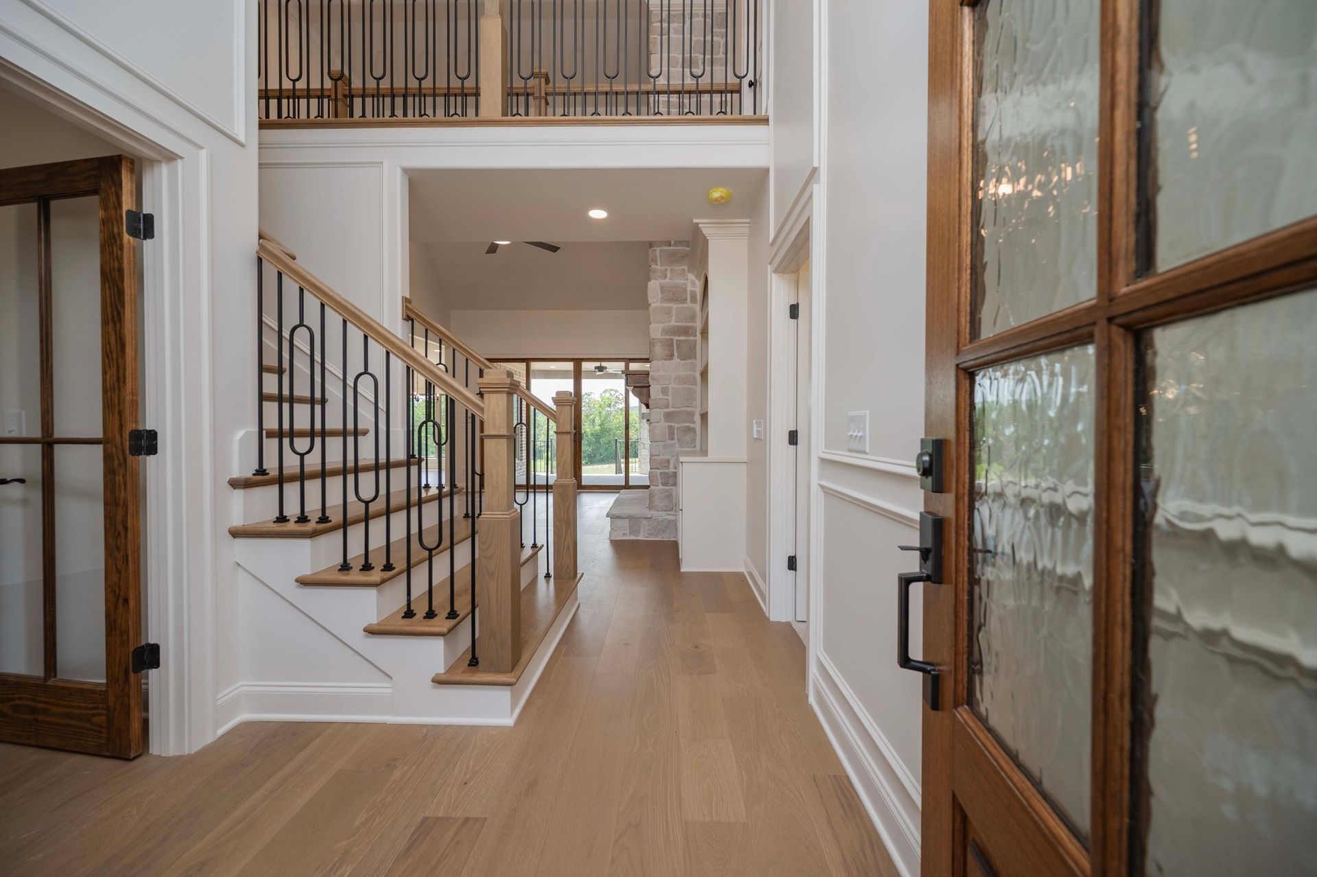 Wooden foyer with stairs, a door, and a view into another room.