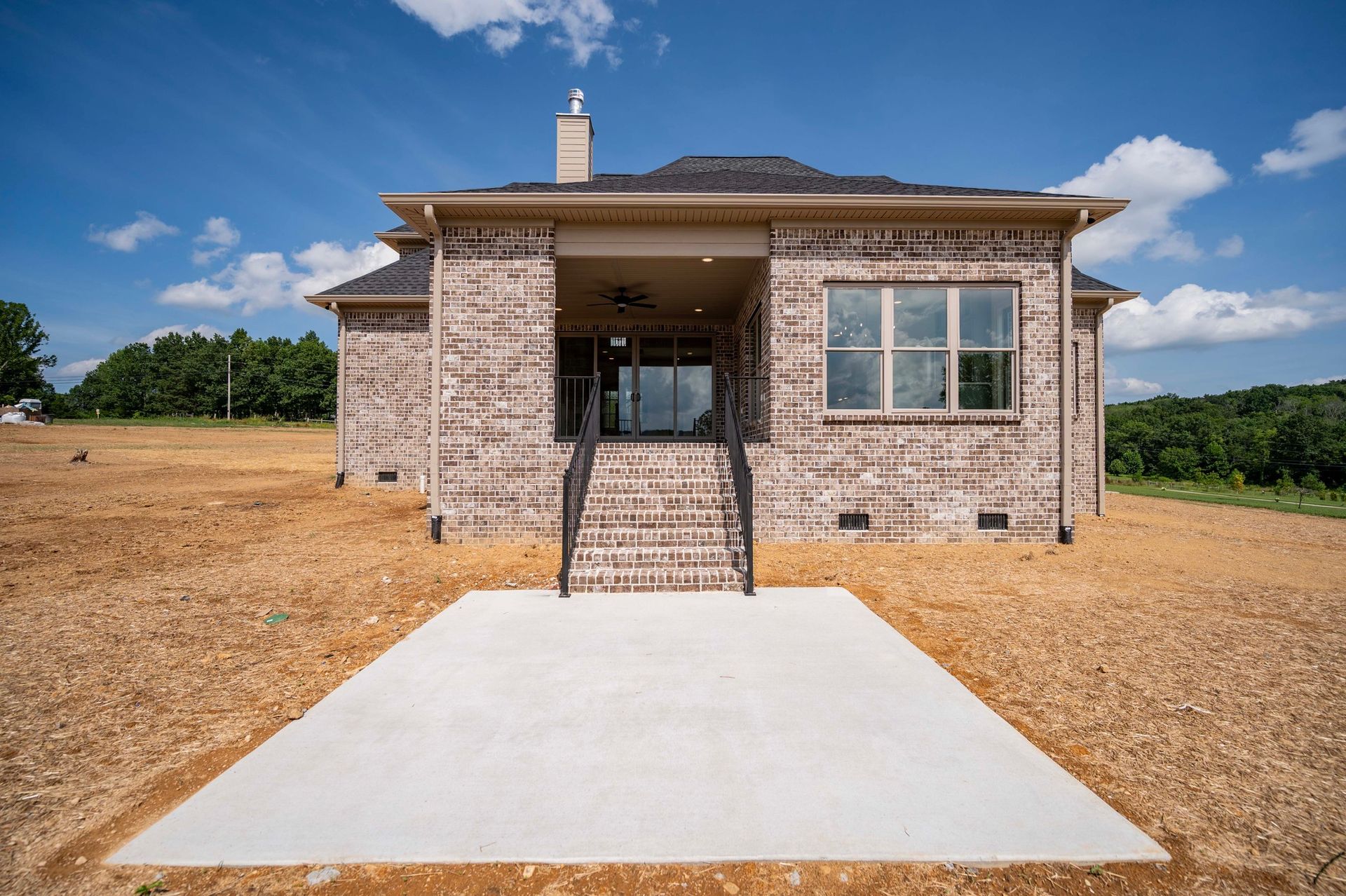 Back of a brick house with concrete patio, steps leading to a covered porch, blue sky.