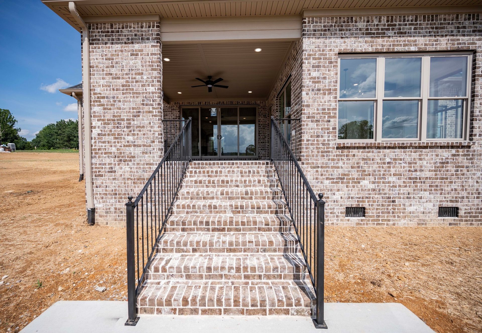 Brick home entryway with steps, black railing, glass door and large window.