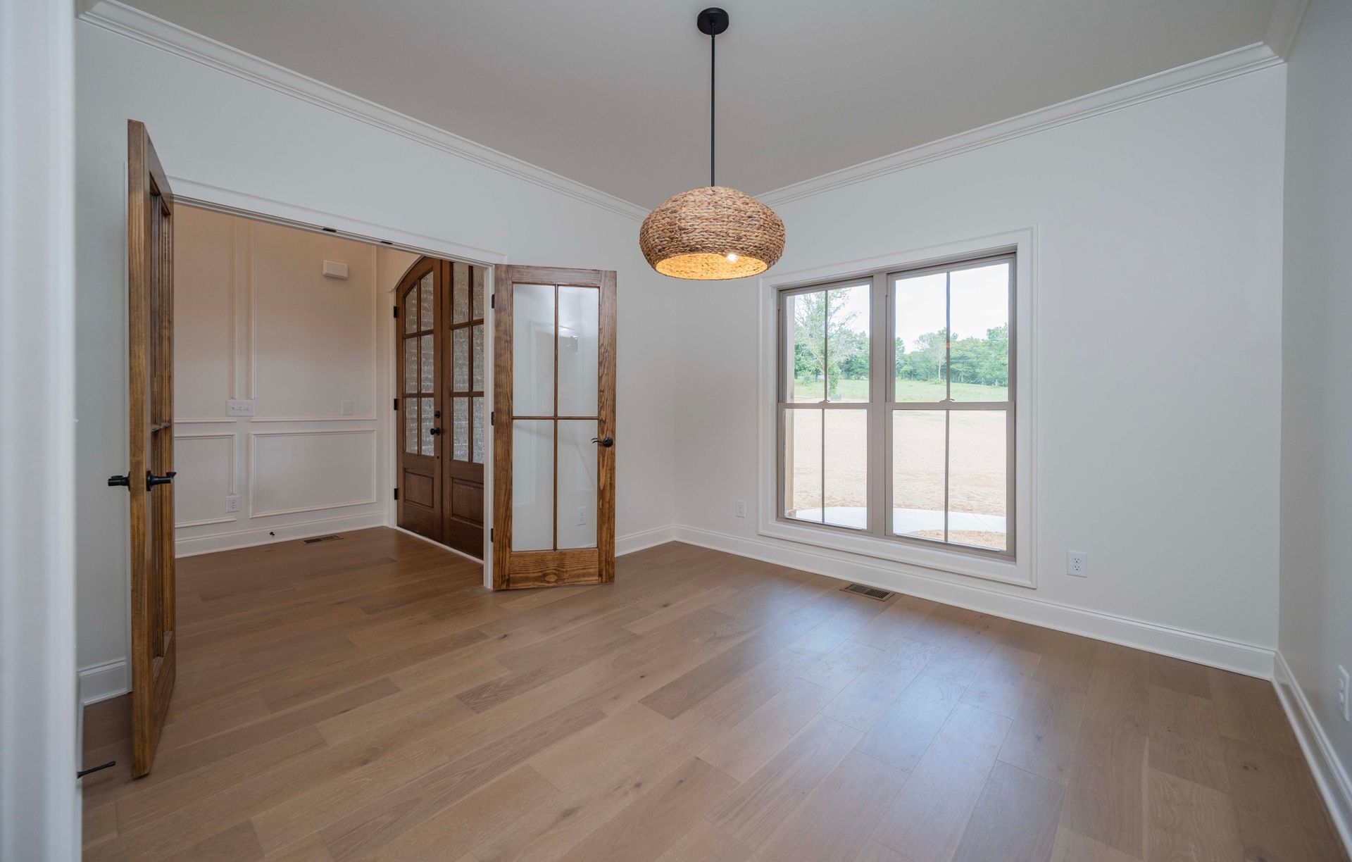 Empty room with hardwood floors, white walls, and a hanging woven light fixture.