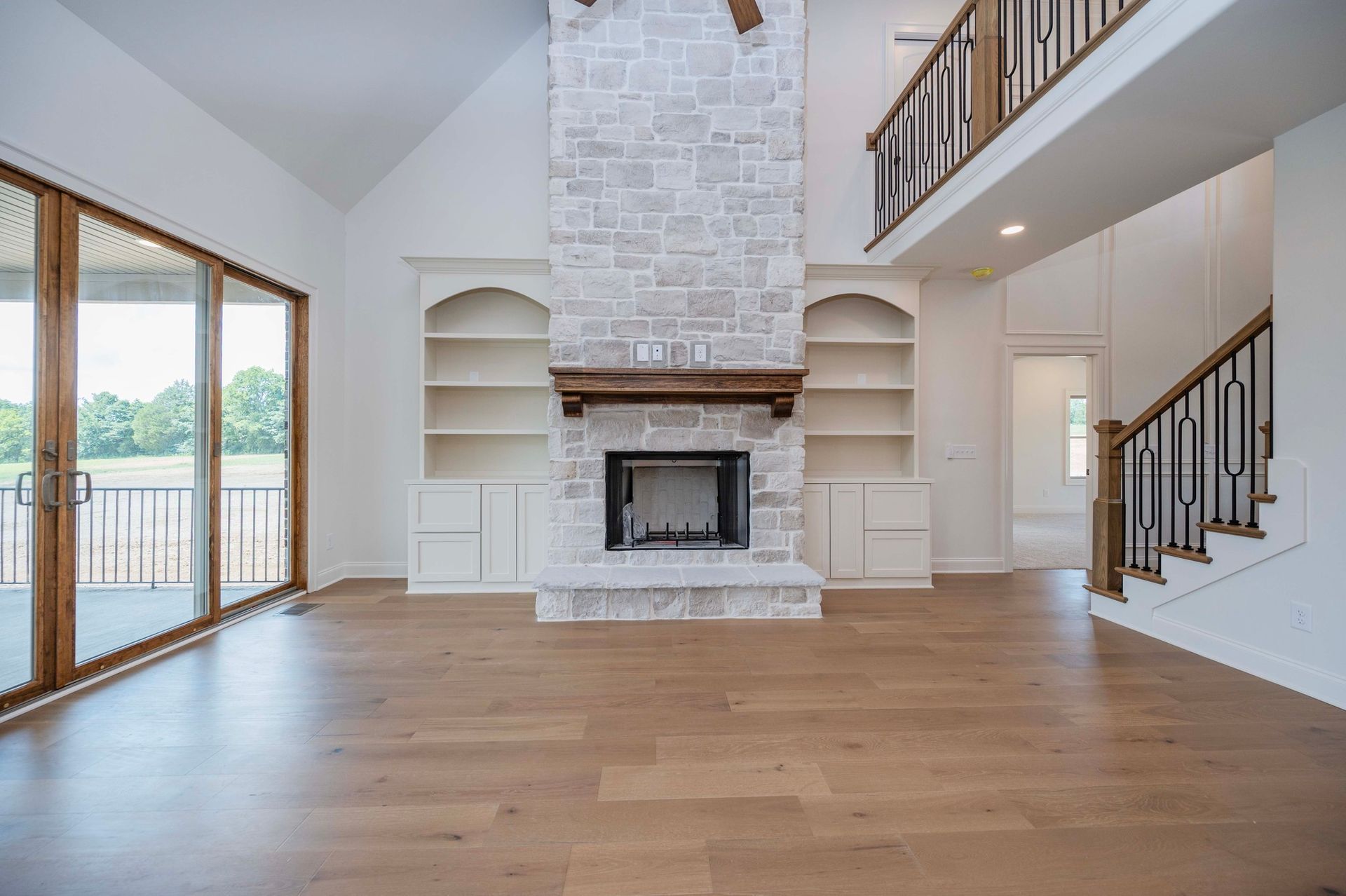 Spacious, light-filled living room with stone fireplace, built-in shelves, and wood floors. Sliding glass doors lead to patio.