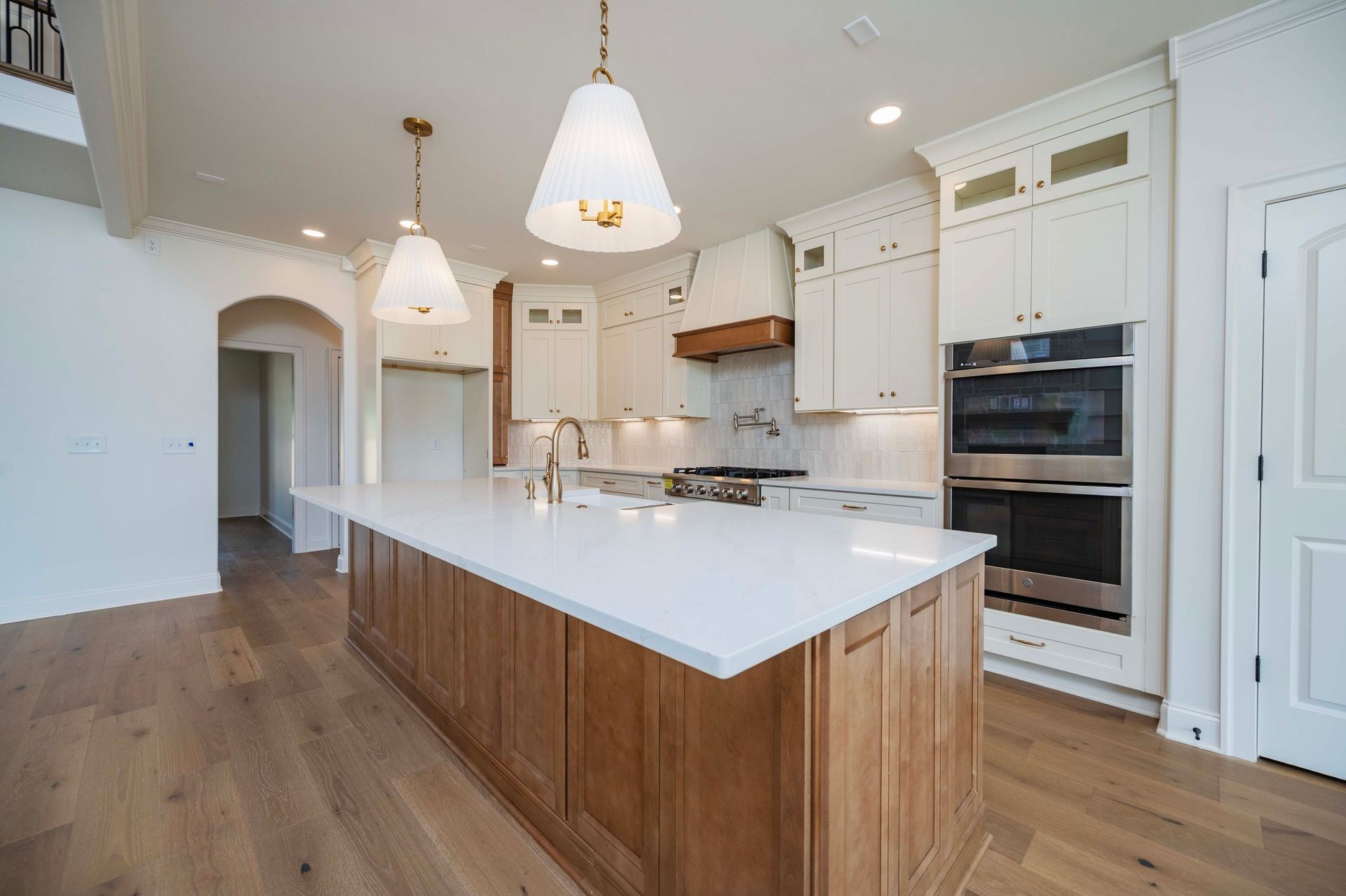 Modern kitchen with white countertops and cabinets, wooden island, hardwood floors, and pendant lights.