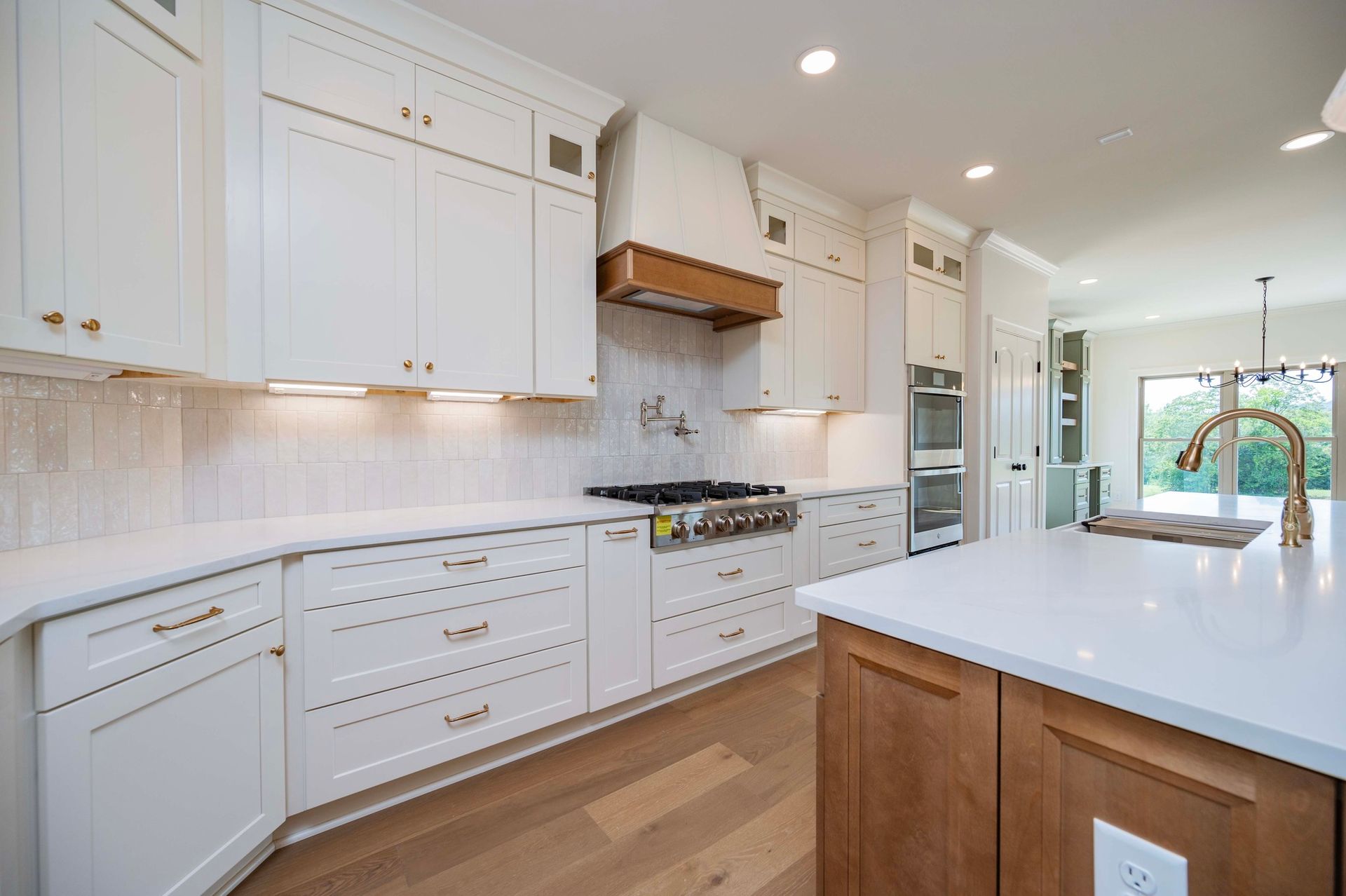 White kitchen with light wood floor, cabinets, and island; stainless steel appliances.