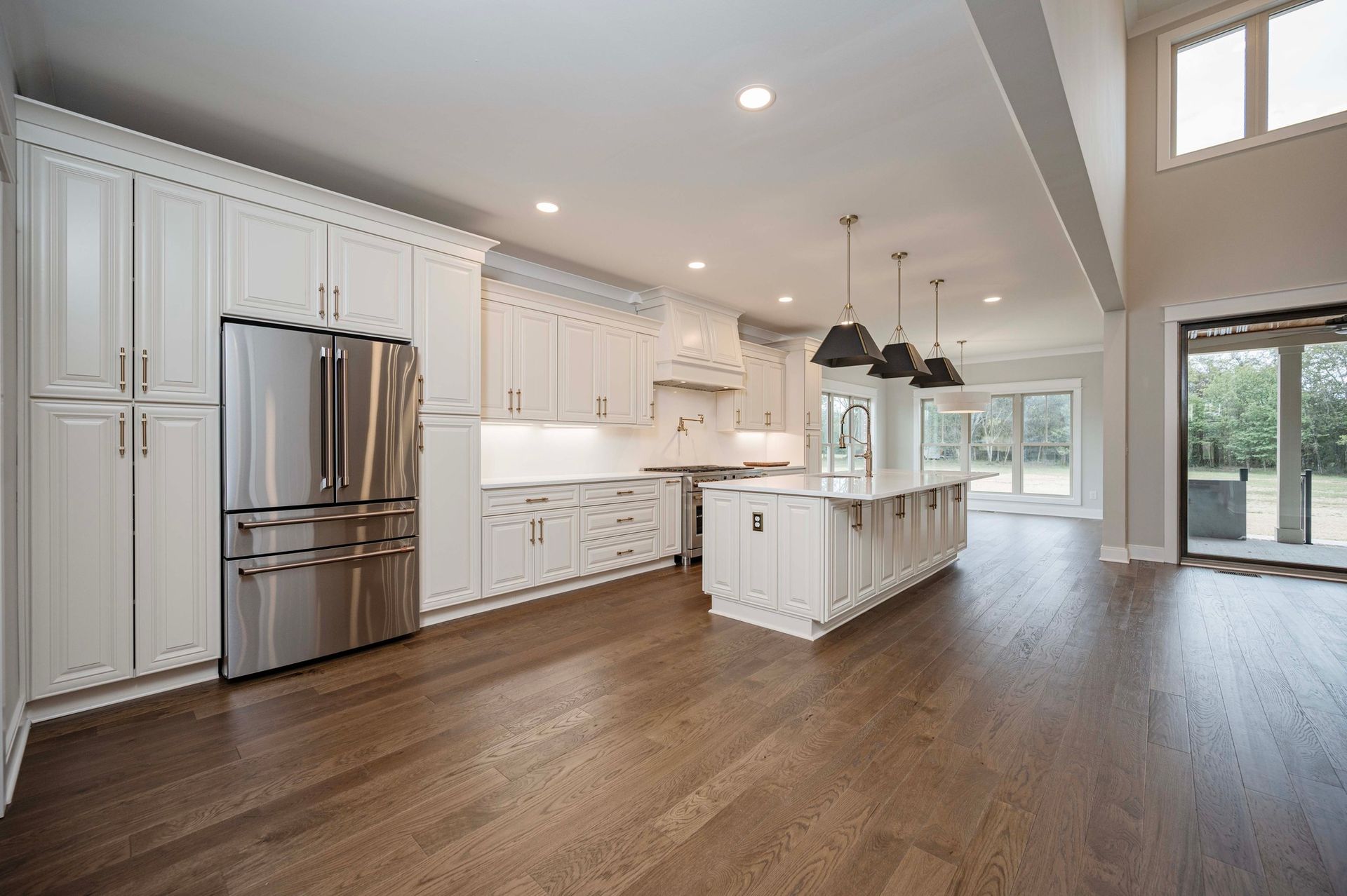 Spacious white kitchen with stainless steel appliances, a large island, hardwood floors, and access to the backyard.