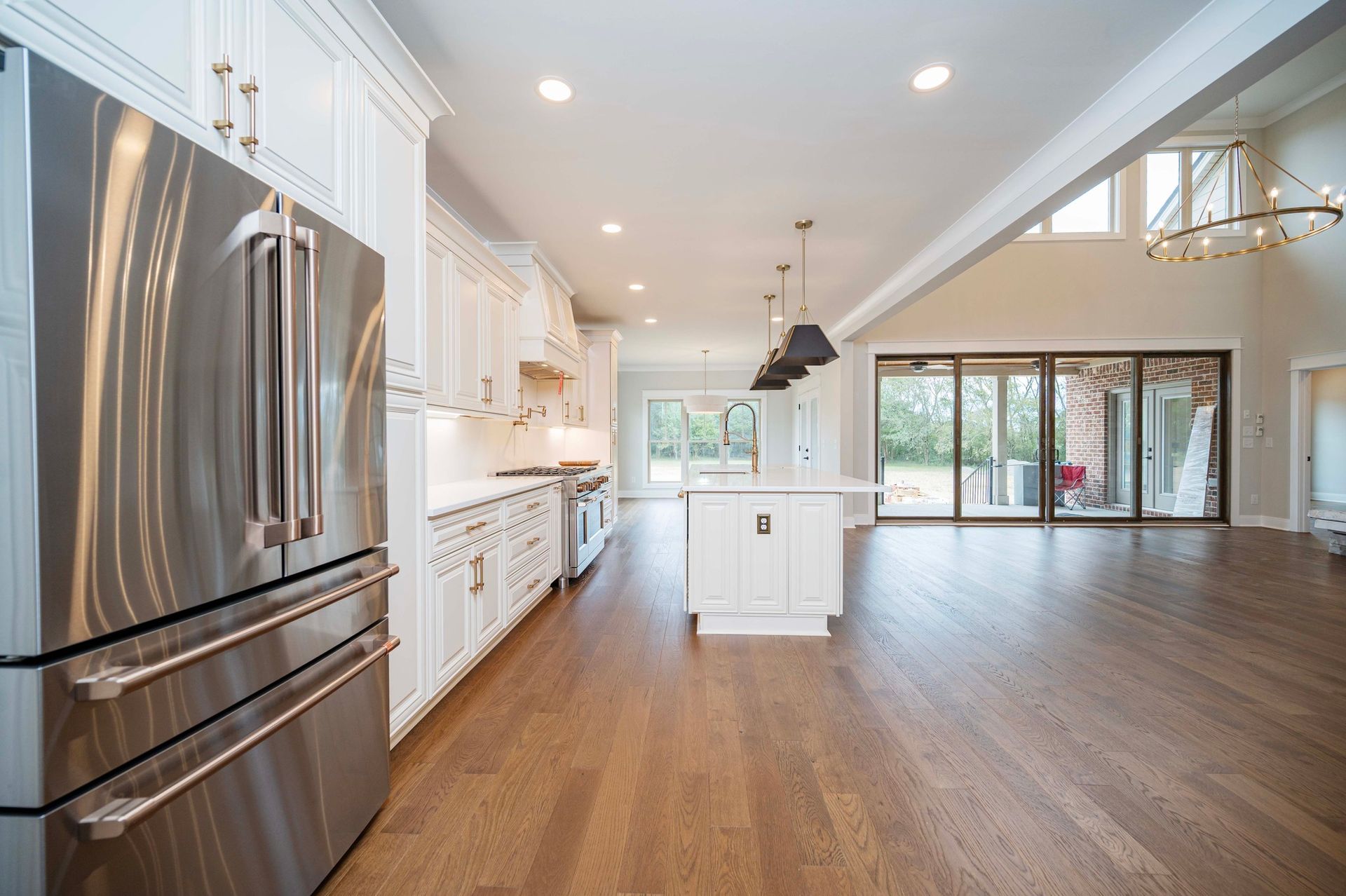 Modern white kitchen with stainless steel appliances, dark wood floors, and open to a backyard.