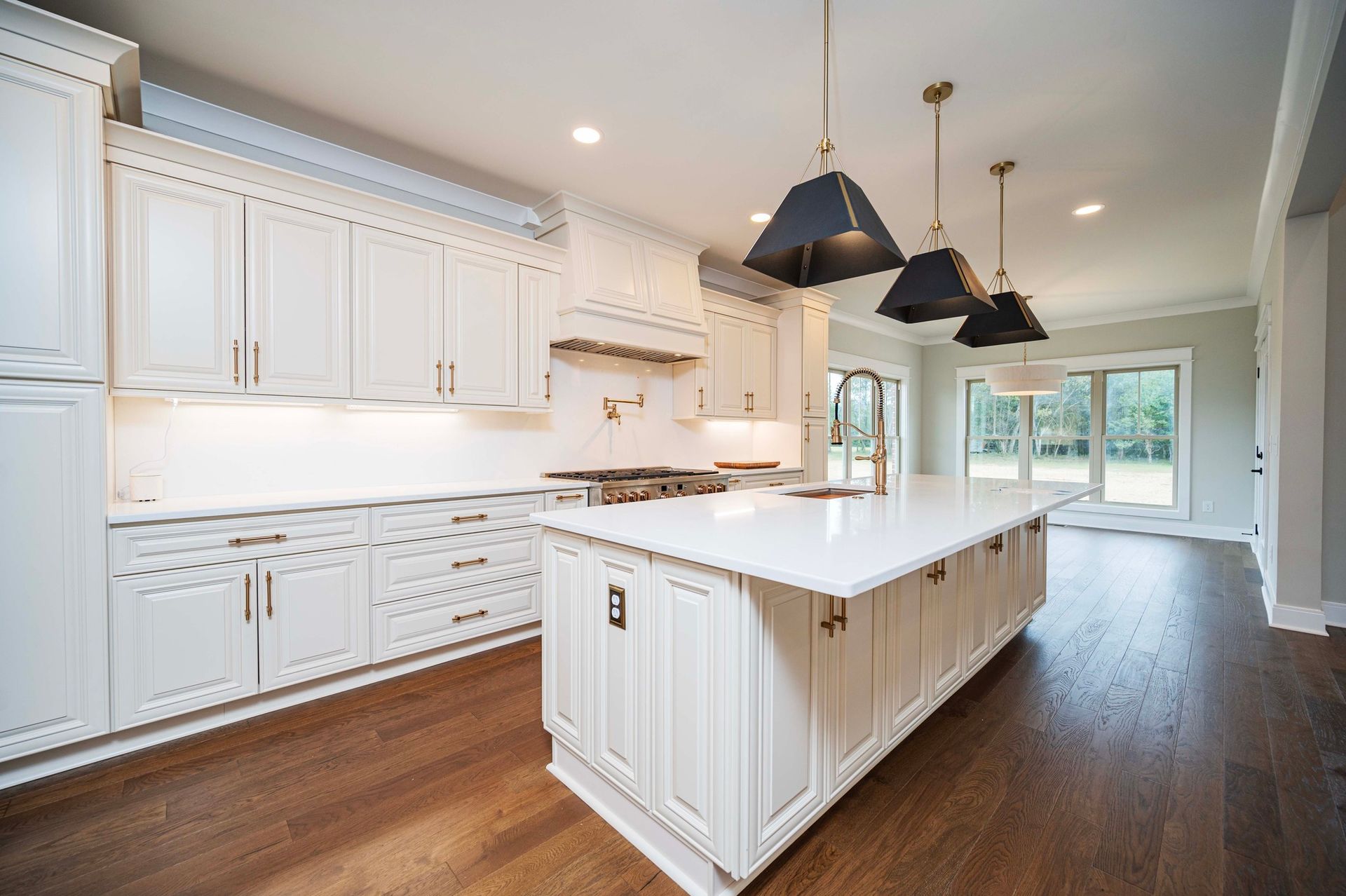 White kitchen with island, cabinets, dark pendant lights, and hardwood floors.
