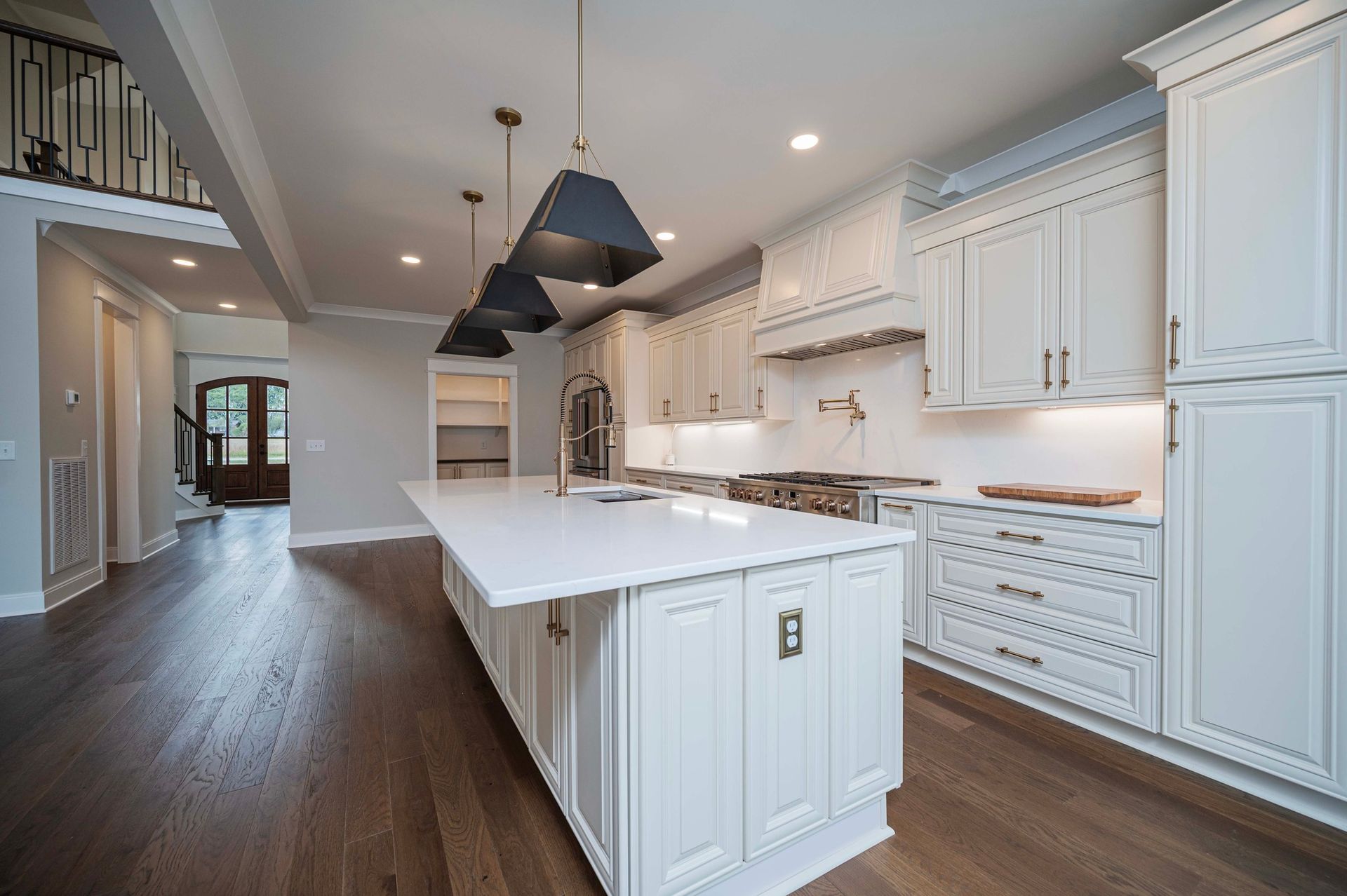 Spacious white kitchen with island and pendant lights. Dark wood floors.