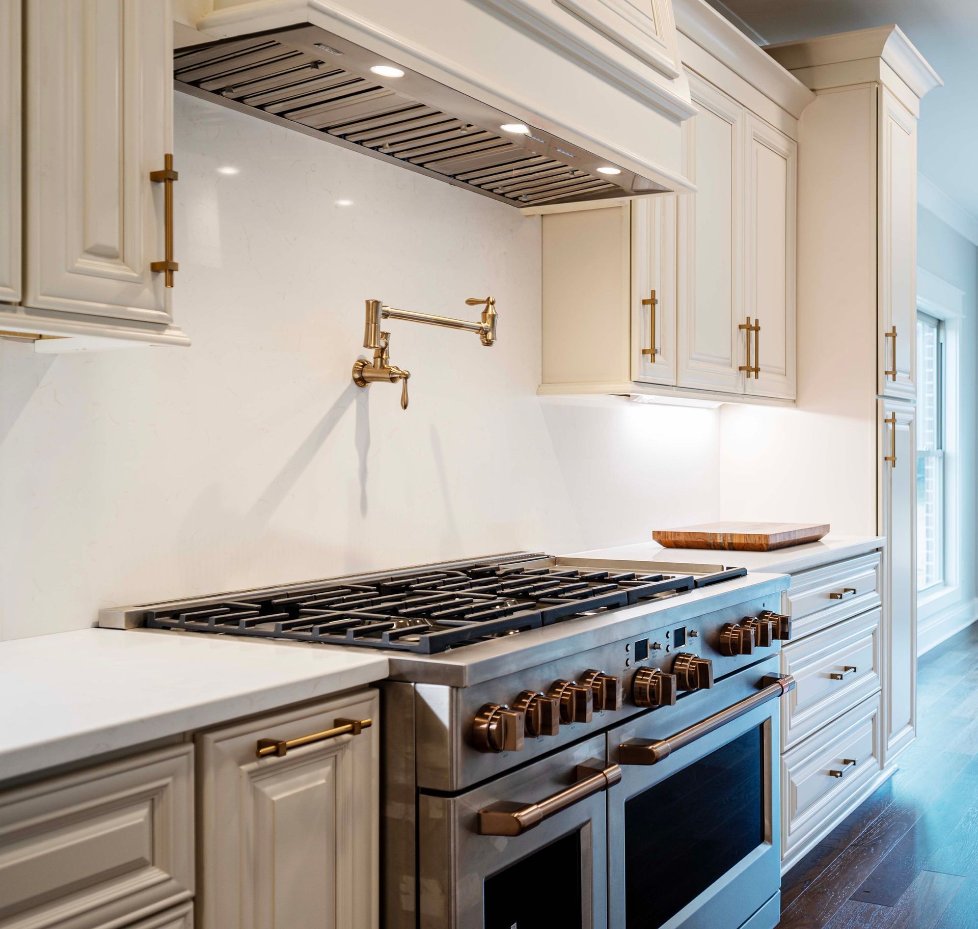Cream-colored kitchen cabinets and stove. Stainless steel range and faucet with bronze hardware.