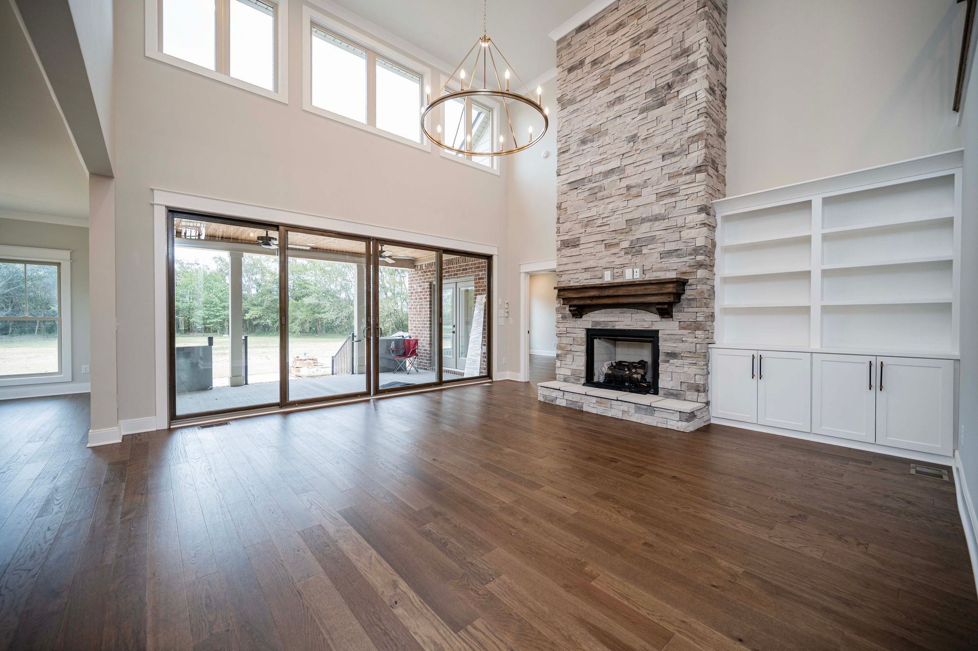 Spacious living room with hardwood floors, a stone fireplace, large windows, and built-in shelving.