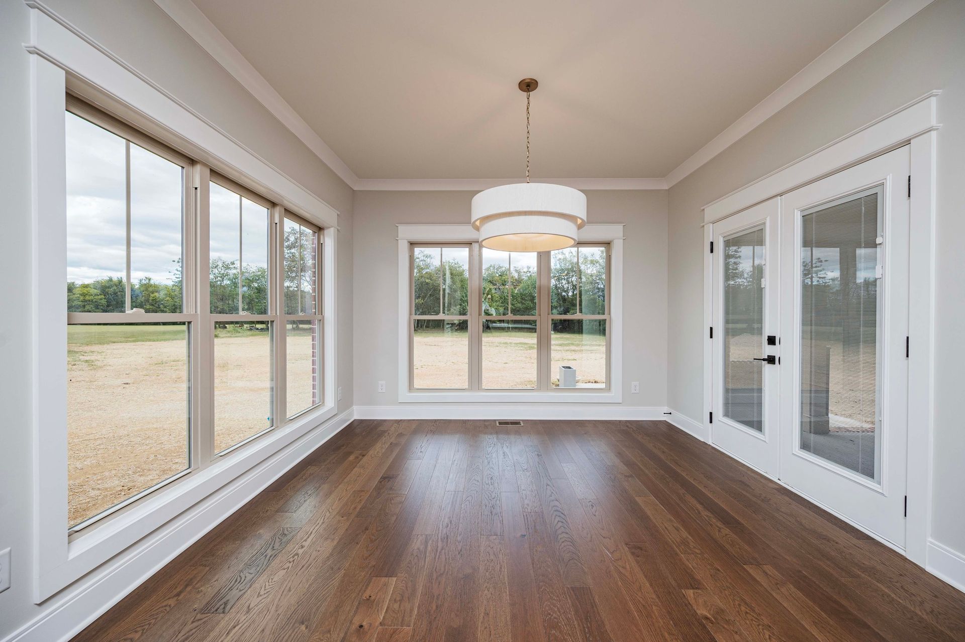Empty room with hardwood floors, large windows, and a pendant light.