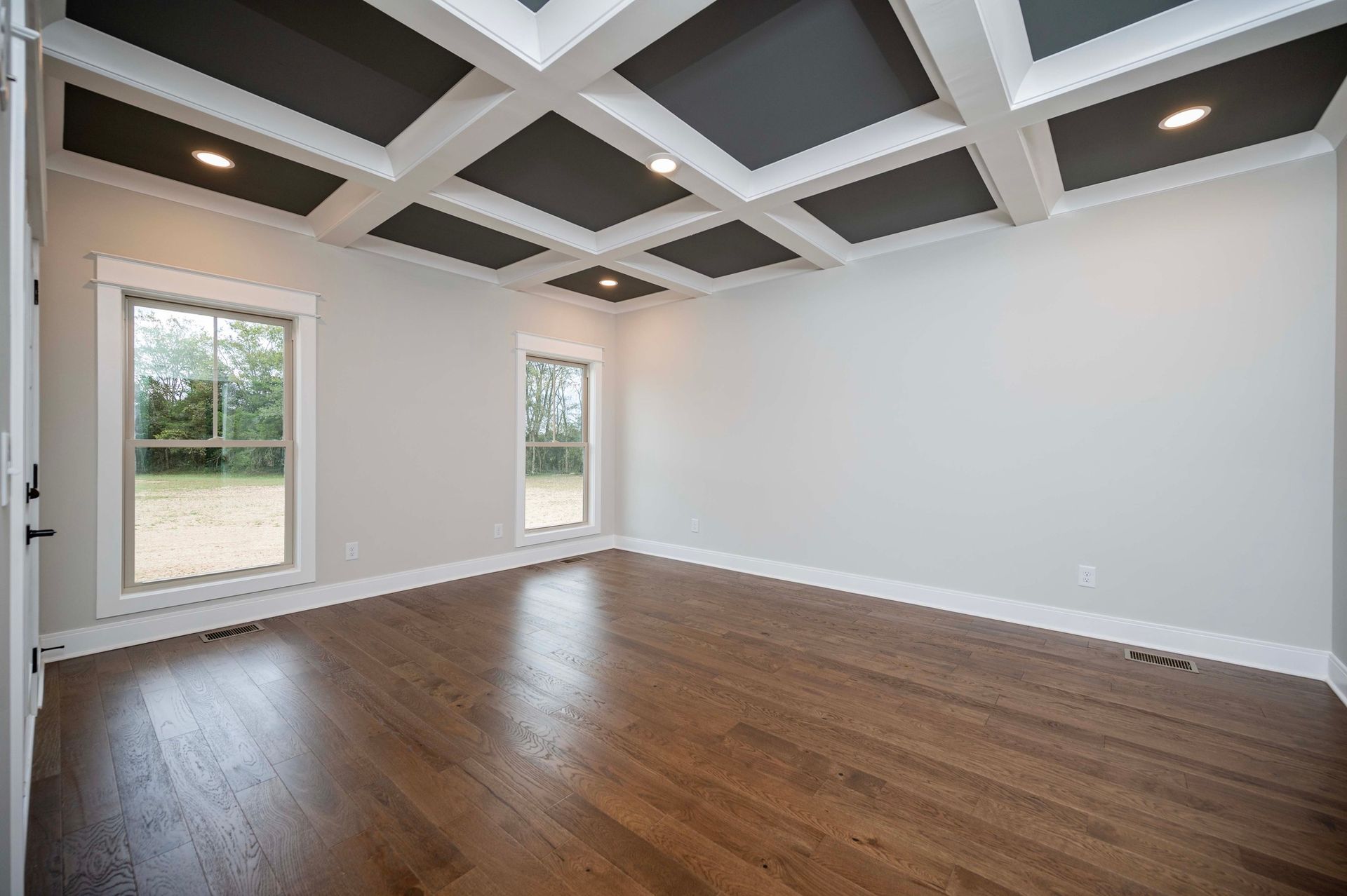 Empty room with dark wood floors, light gray walls, and a coffered ceiling with dark gray panels.