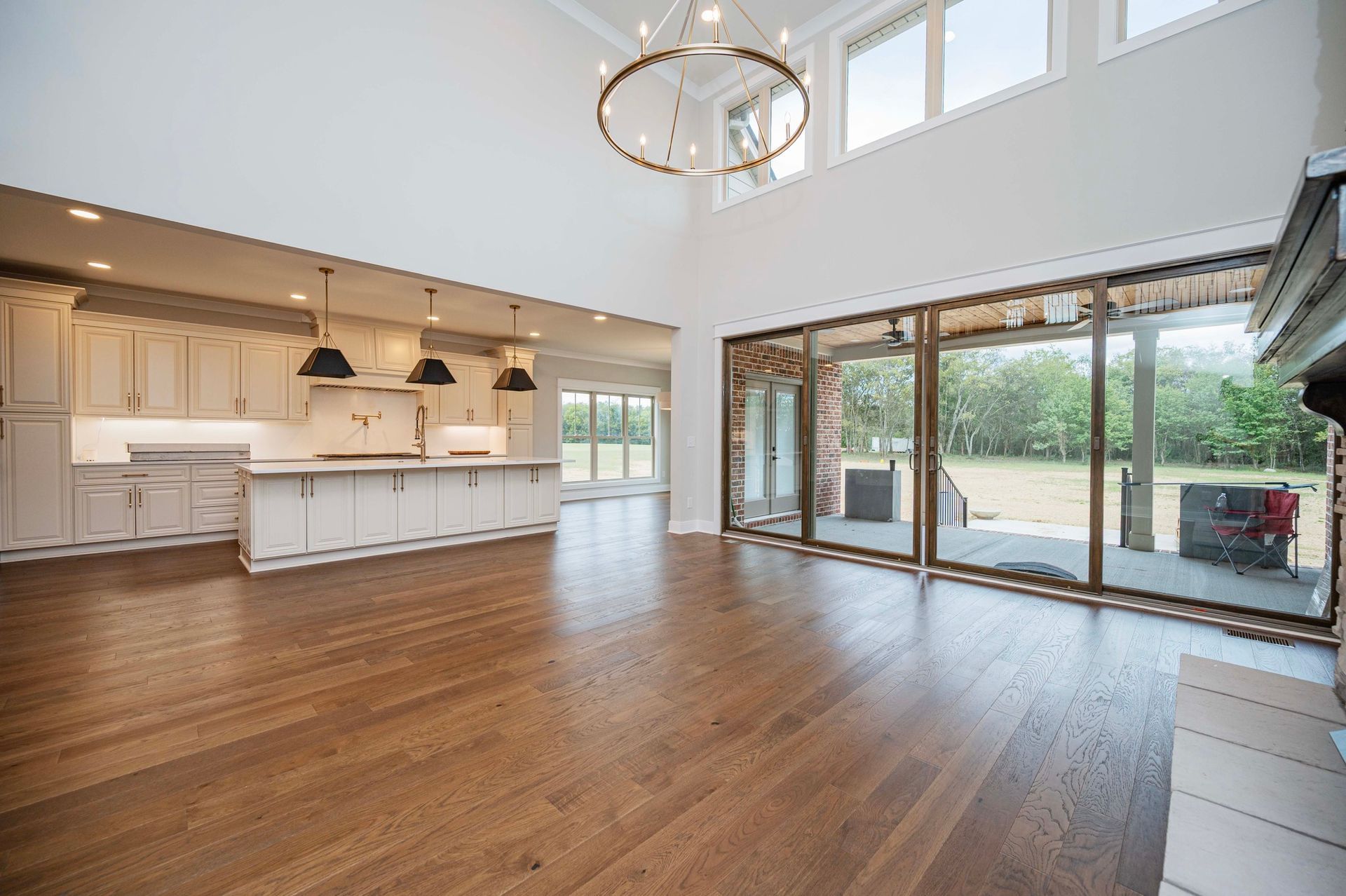 Spacious living area with hardwood floors, a kitchen, and large windows overlooking a backyard.