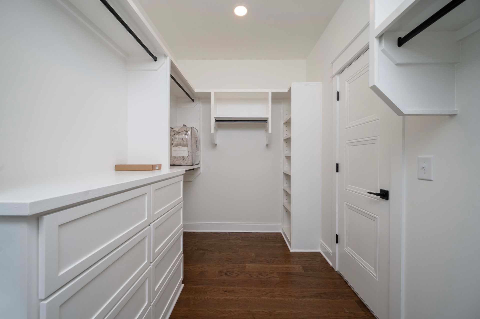 Walk-in closet with white shelving, cabinets, and door, and hardwood flooring.