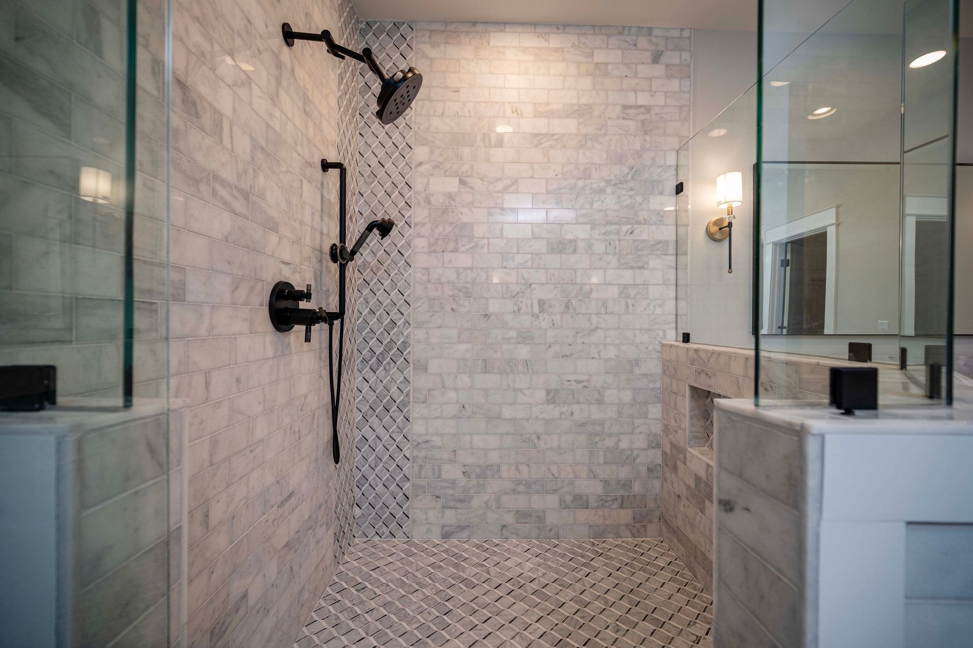 Spacious, modern shower with glass doors, marble tile walls, and dark fixtures.