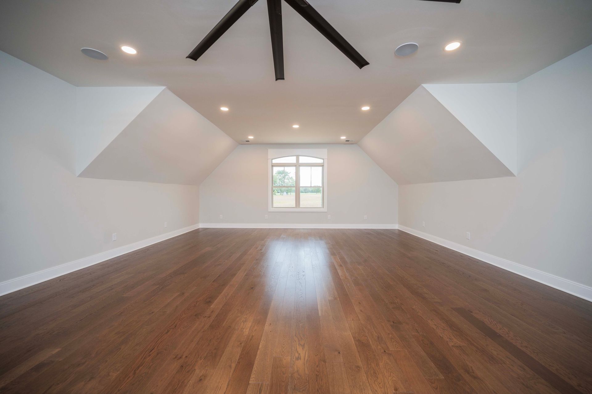 Empty room with hardwood floors, white walls, angled ceiling, and a window.