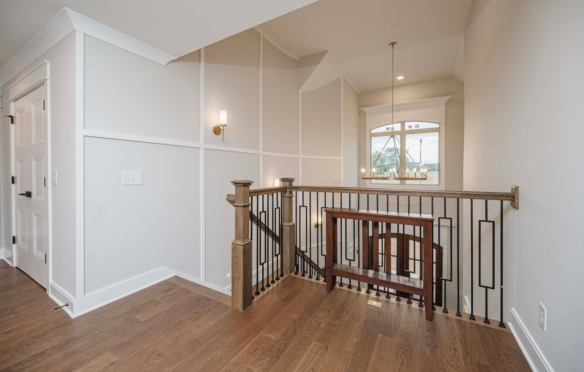 Hallway with wood floors, railing, white walls with trim, and a small table.