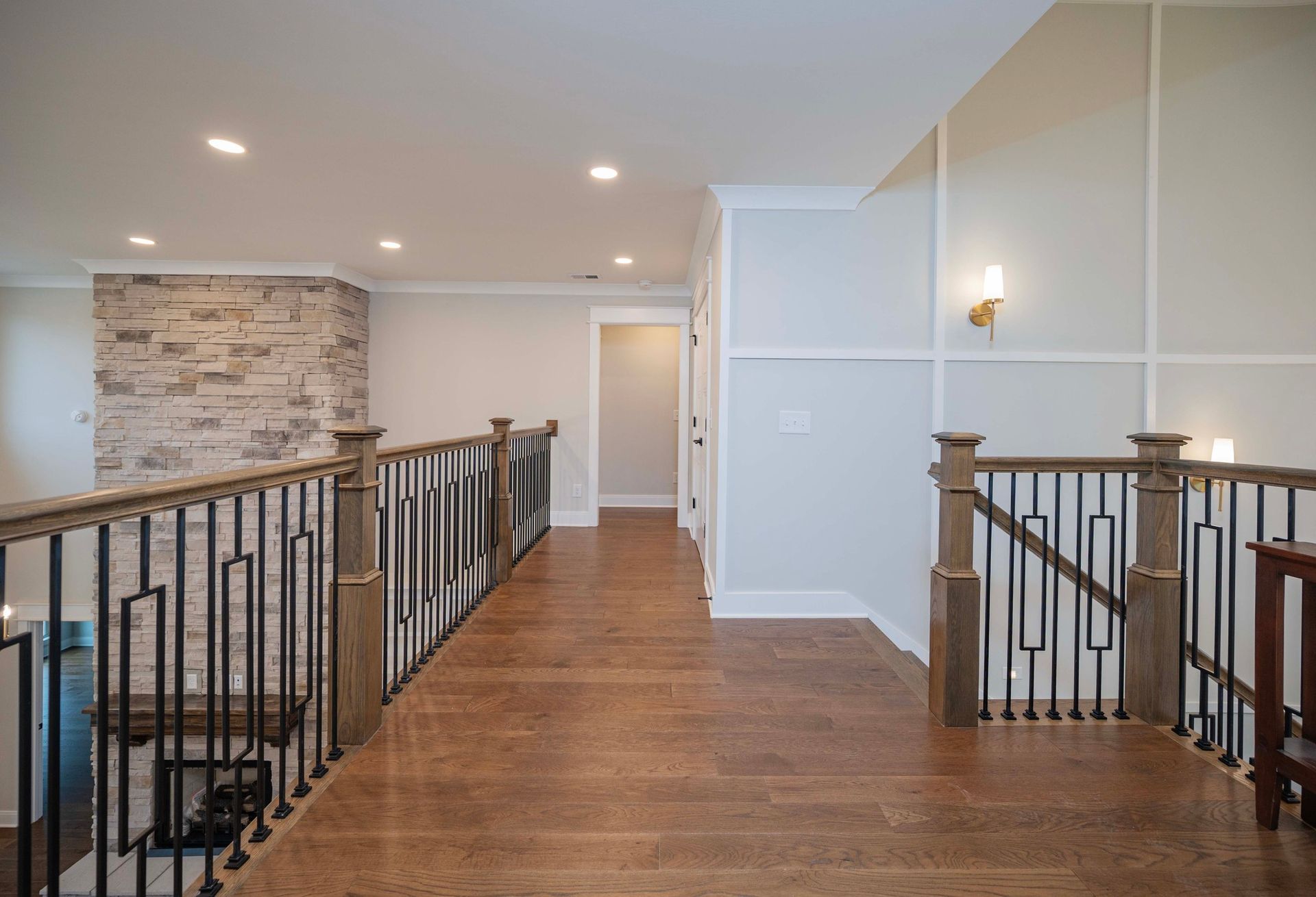 A hallway with hardwood floors, a stone wall, and a staircase with black iron railings and wooden posts.