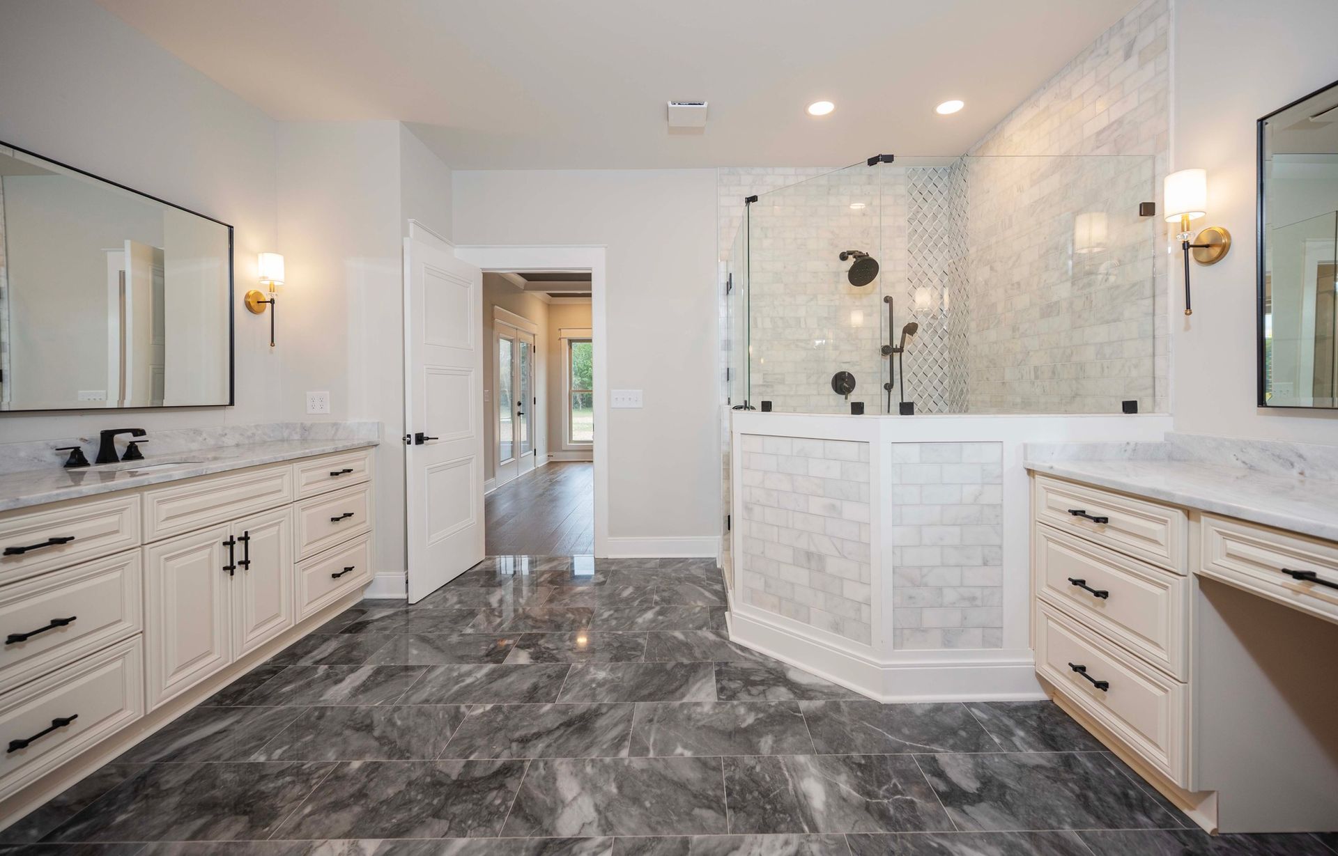 Spacious bathroom with gray marble floor, white cabinets, and glass shower.