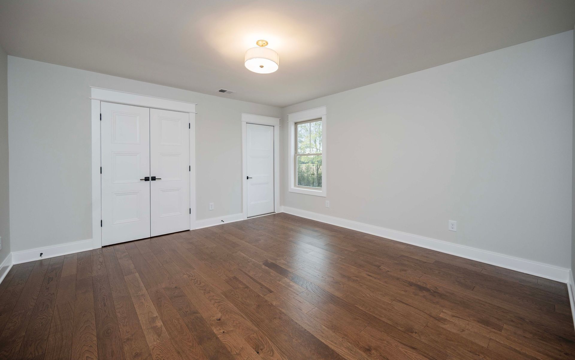 Empty room with hardwood floors, white doors, and a small window.