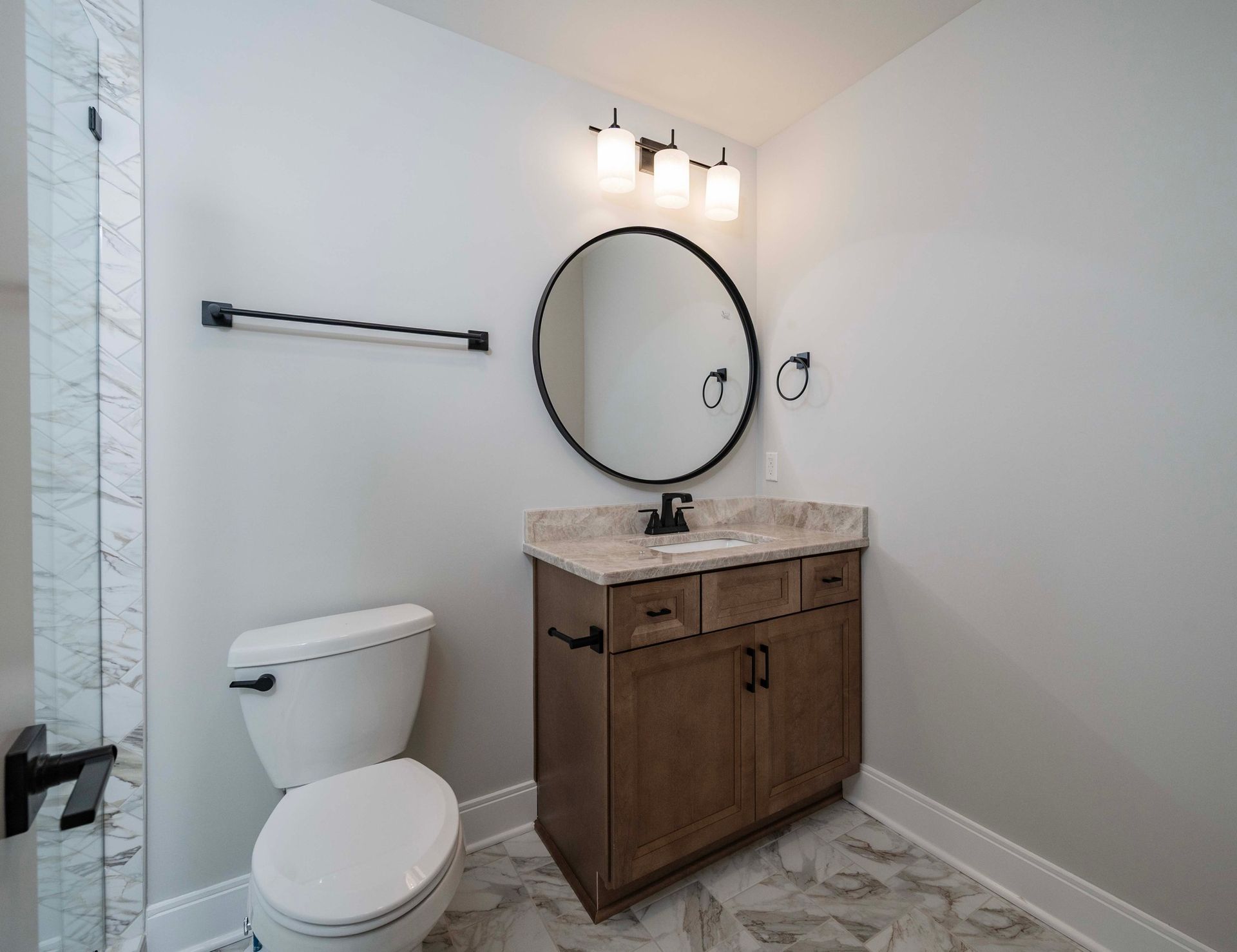 Bathroom with a toilet, vanity with a round mirror, and a towel rack. Gray and brown tones.