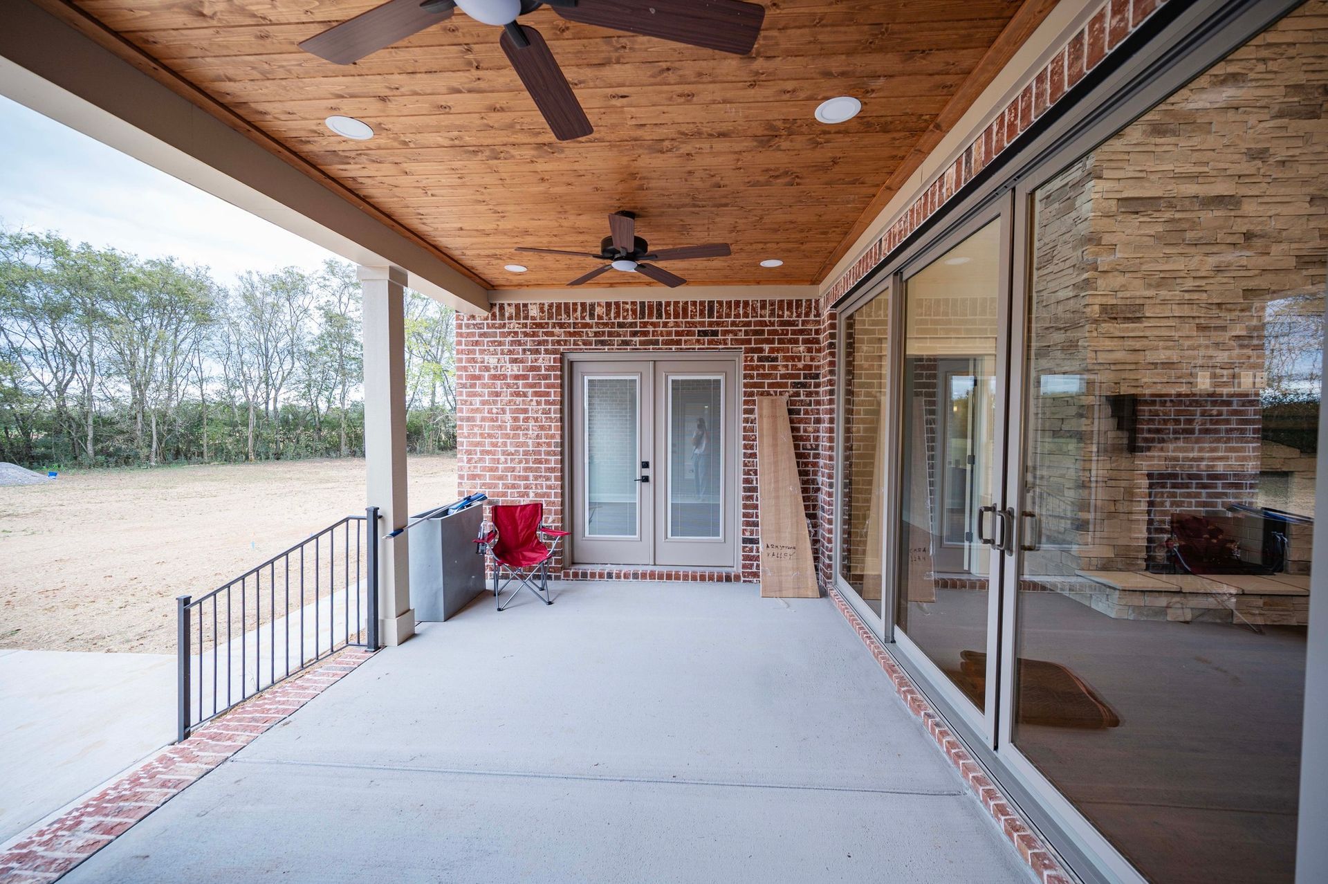 Covered patio with brick walls, sliding glass doors, and a concrete floor. A red chair sits near double doors.