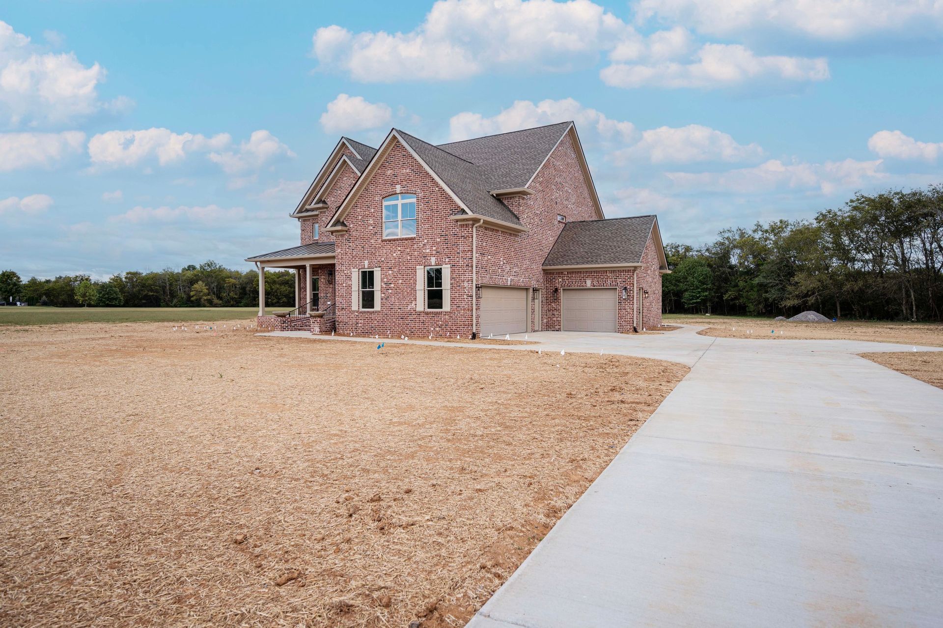 Brick house with attached garage and concrete driveway on a dry, dirt lot under a blue sky.