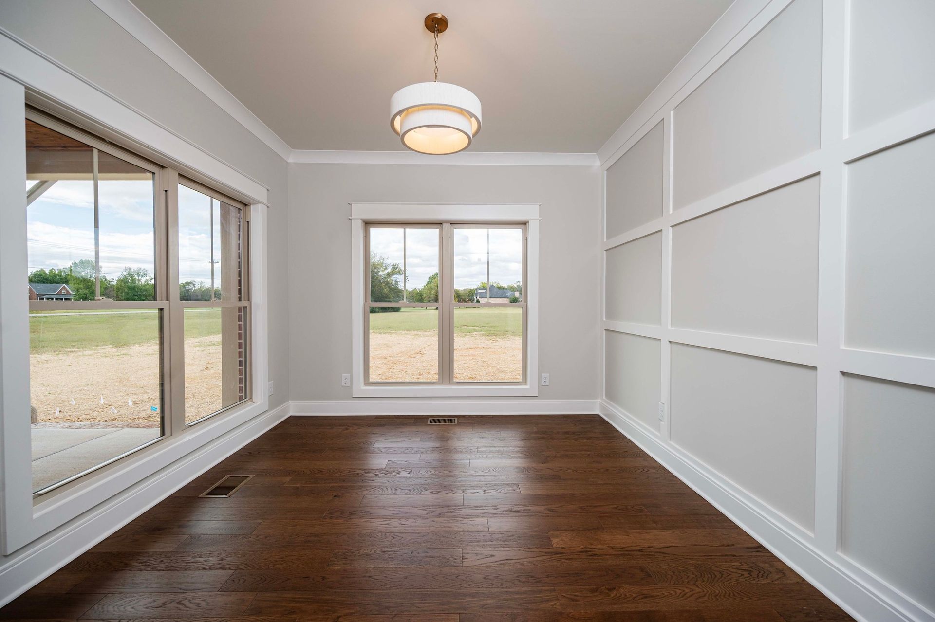 Empty room with dark wood floors, white trim, and grid-paneled walls. Large windows.