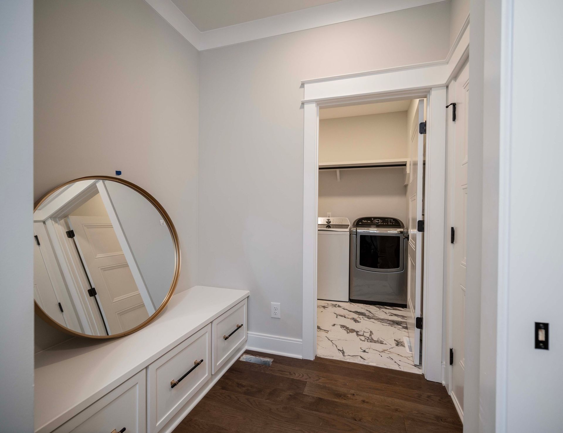 Entryway with bench, round mirror, and view into laundry room with washer and dryer.