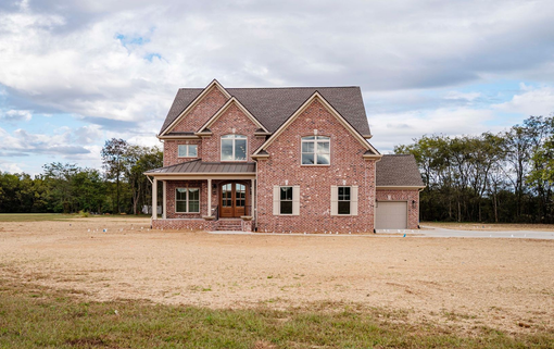 Brick-faced two-story house with a small attached garage and brown roof, set in a field.