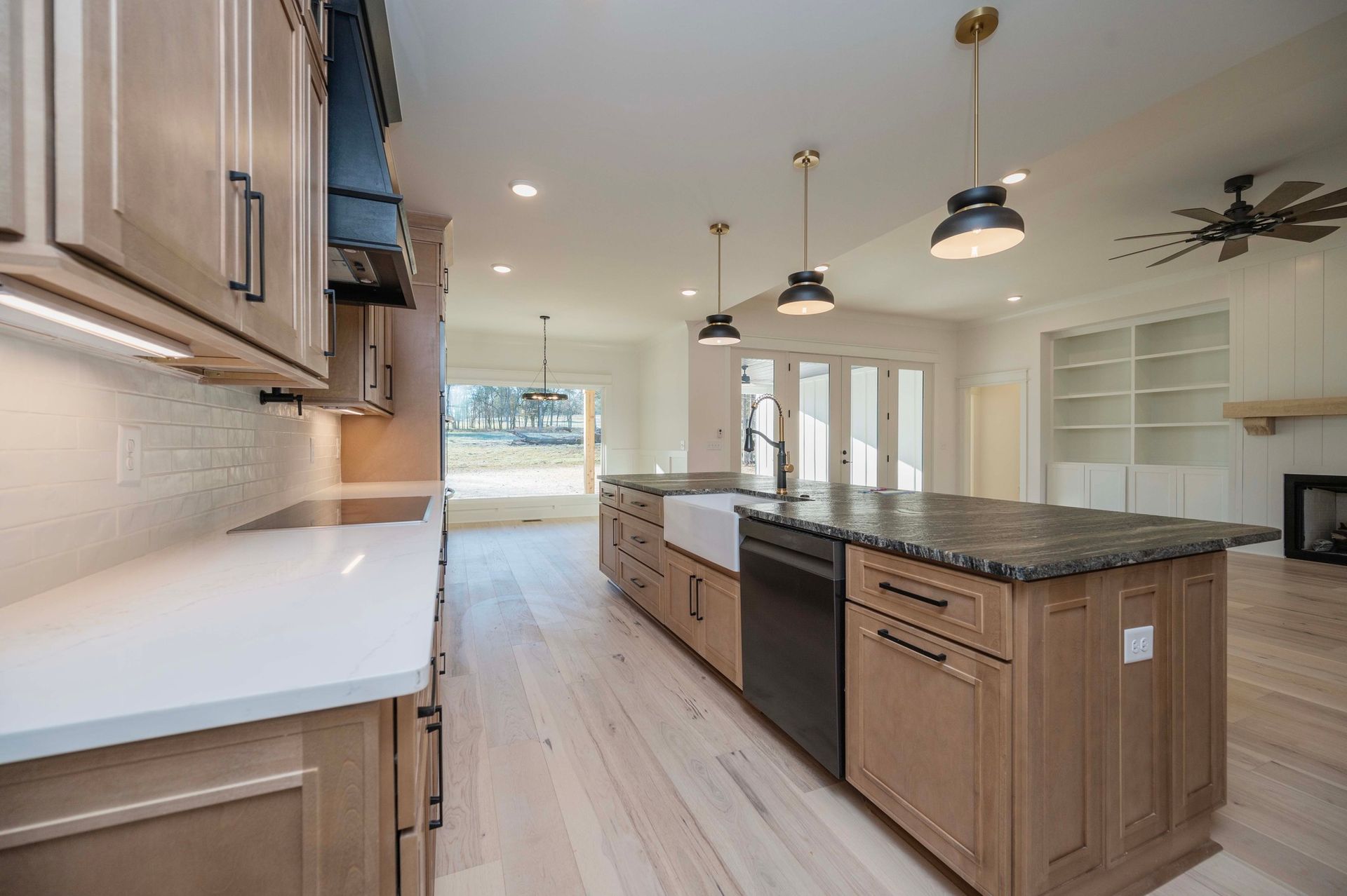 Spacious kitchen with wood cabinets, island, and light wood floors. White countertops and black accents.