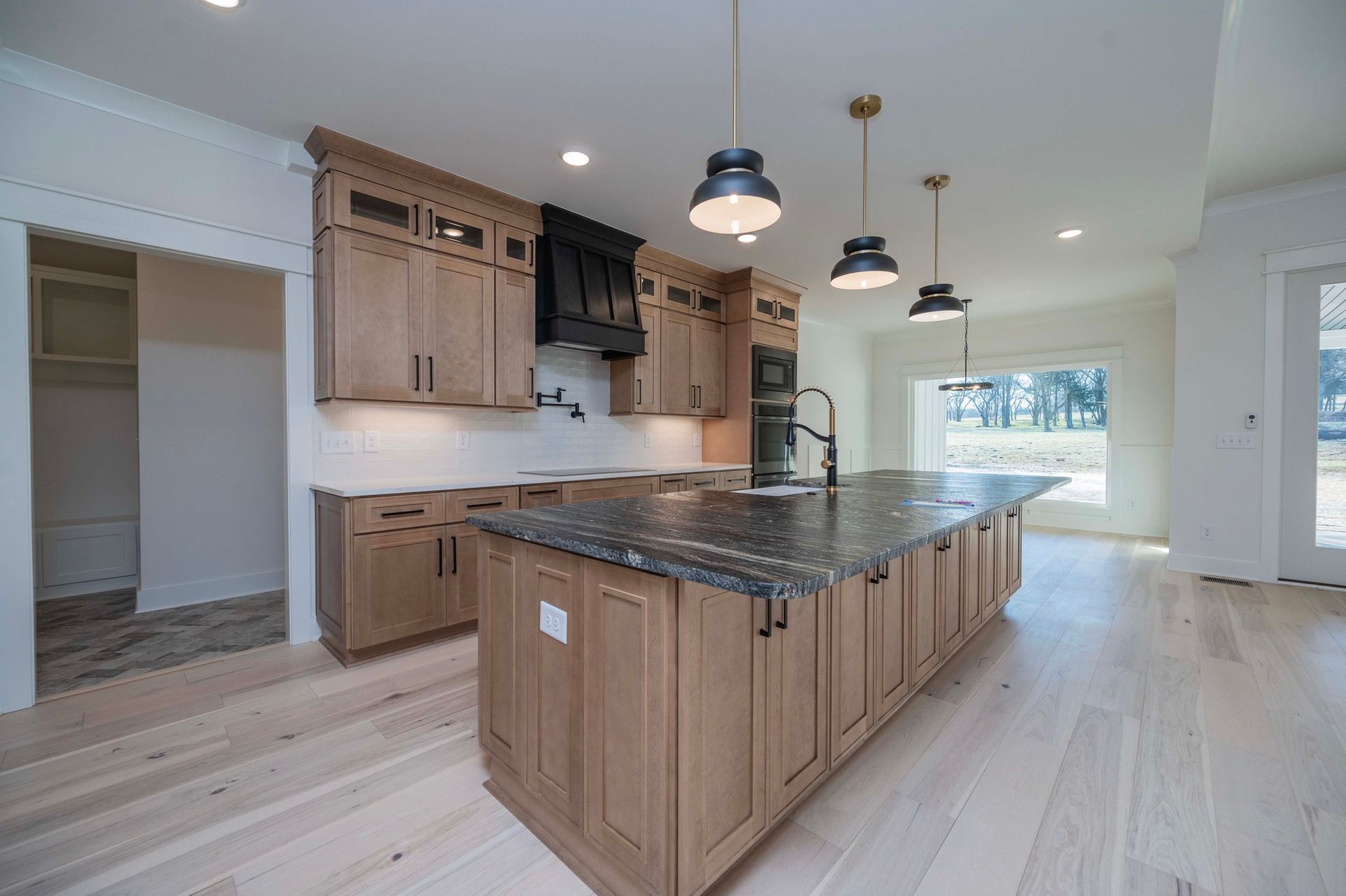 Kitchen with light wood cabinets, dark countertops, and three pendant lights over a large island.