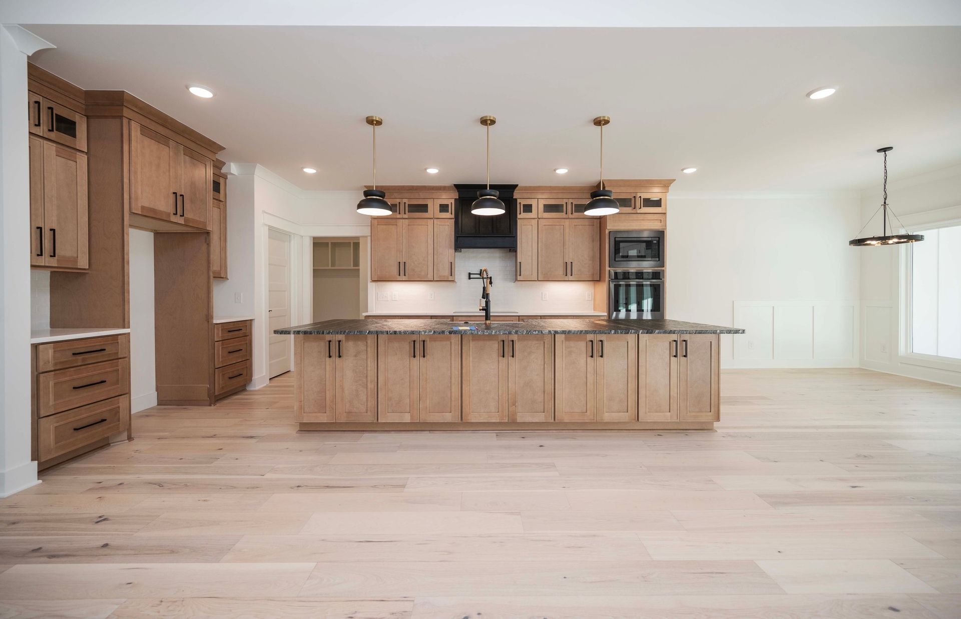 Kitchen with light wood cabinets, dark range hood, island, and light wood floors.