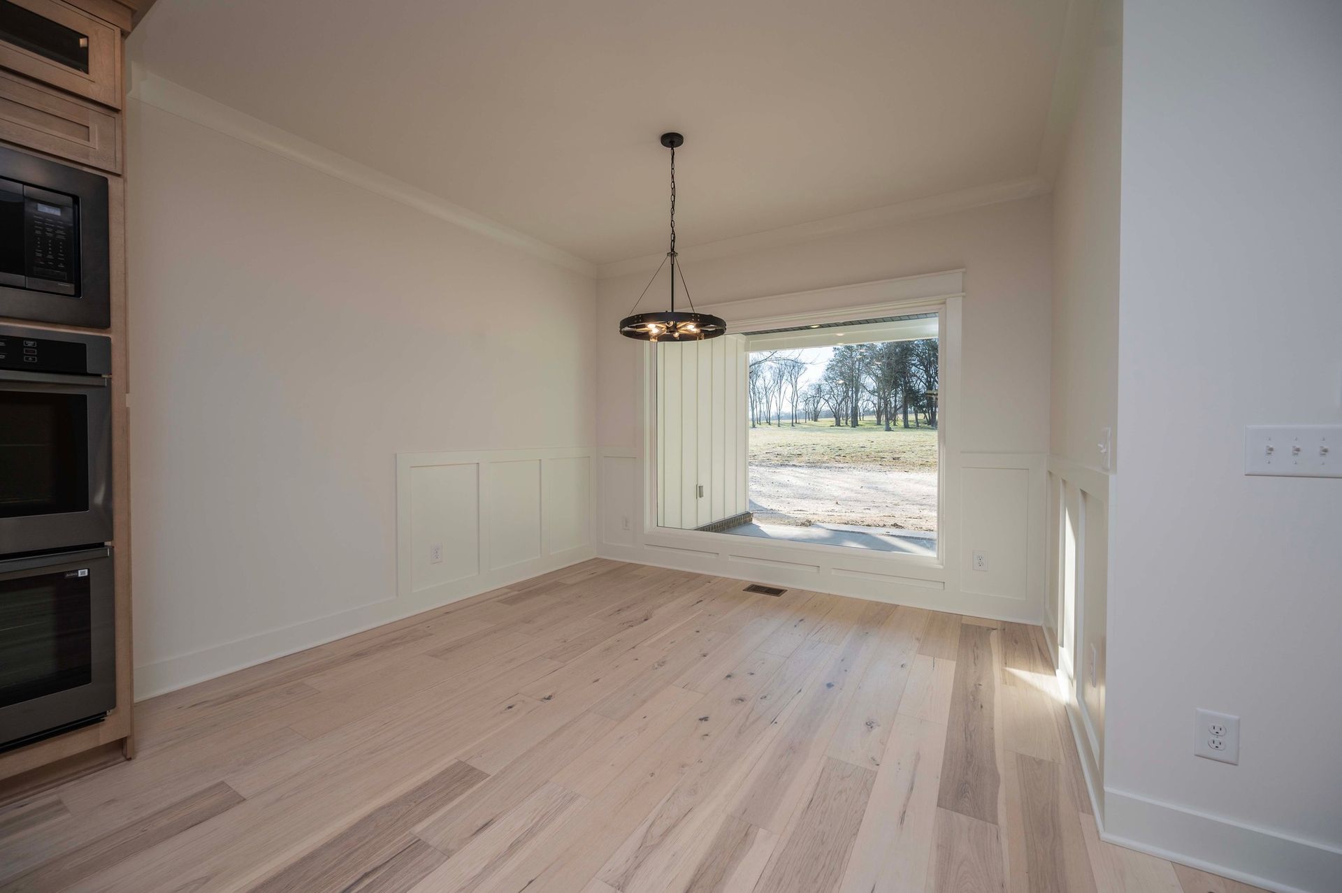 Empty dining room with wood floors, large window, and light fixture.