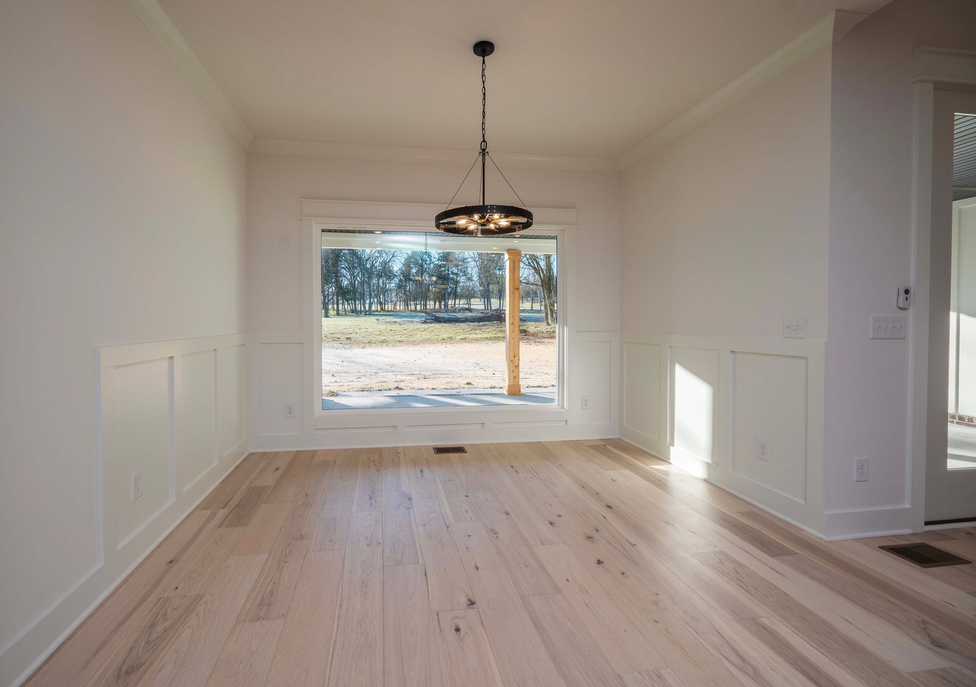 Empty dining room with wooden floor, large window, and chandelier.