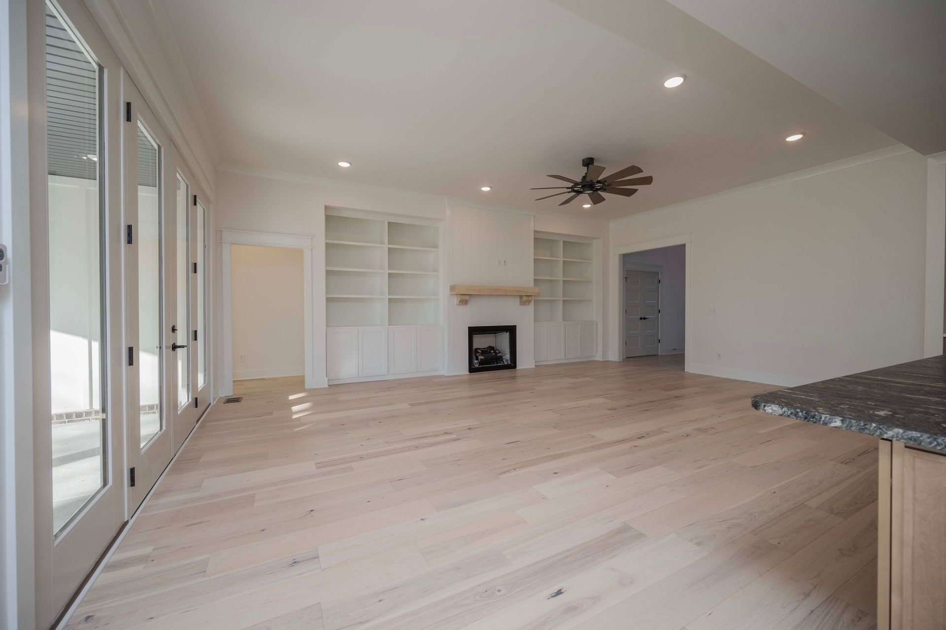 Bright, empty living room with wood floors, built-in shelves, fireplace, and french doors.