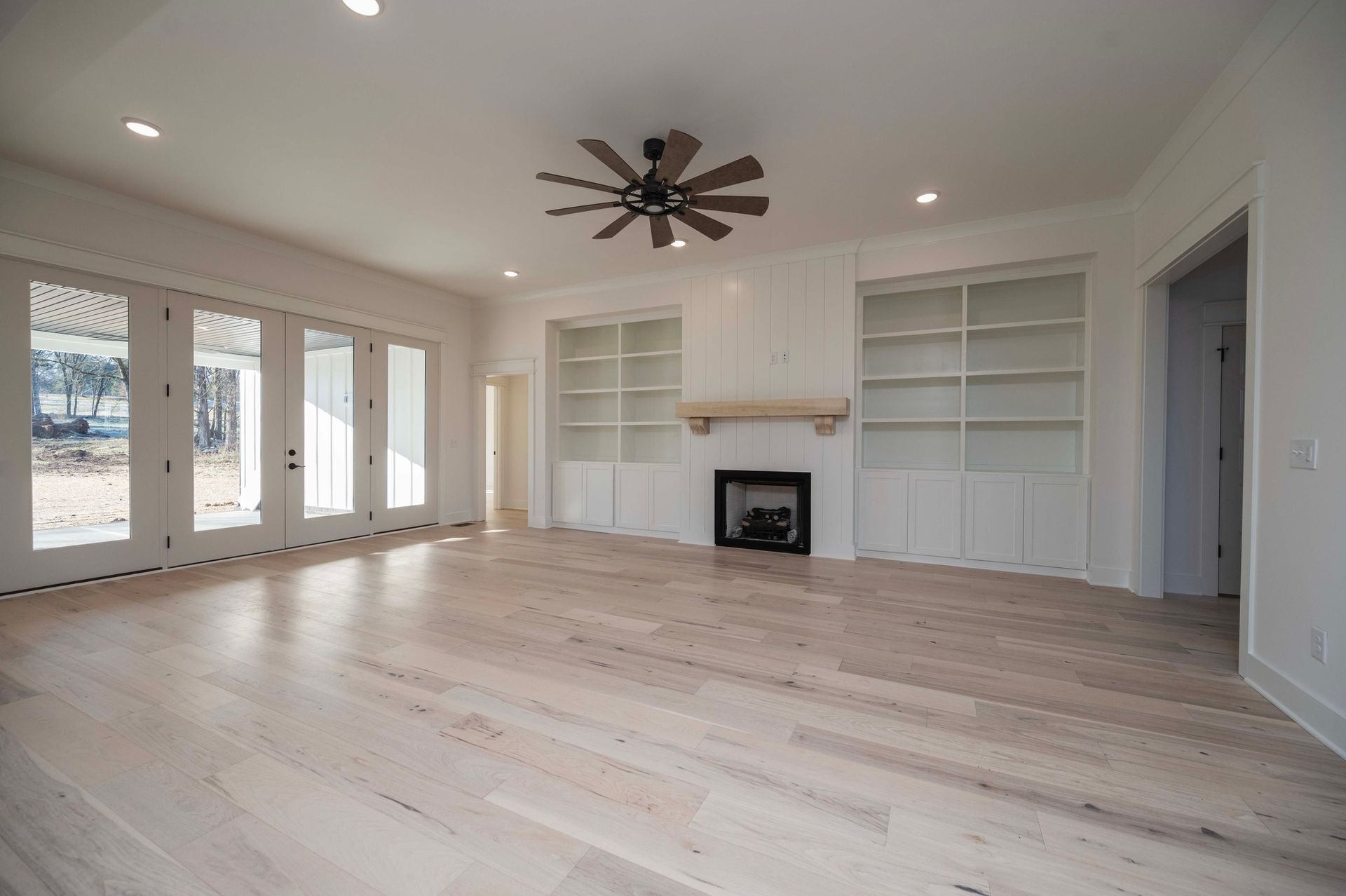 Empty living room with light wood floors, built-in bookshelves, and fireplace.