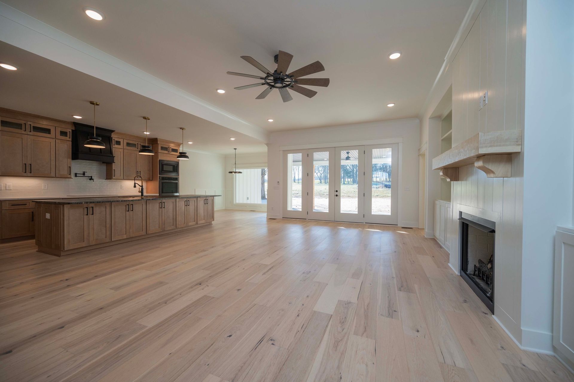 Open-concept living space with kitchen and fireplace. Light wood flooring, neutral tones, and large windows.