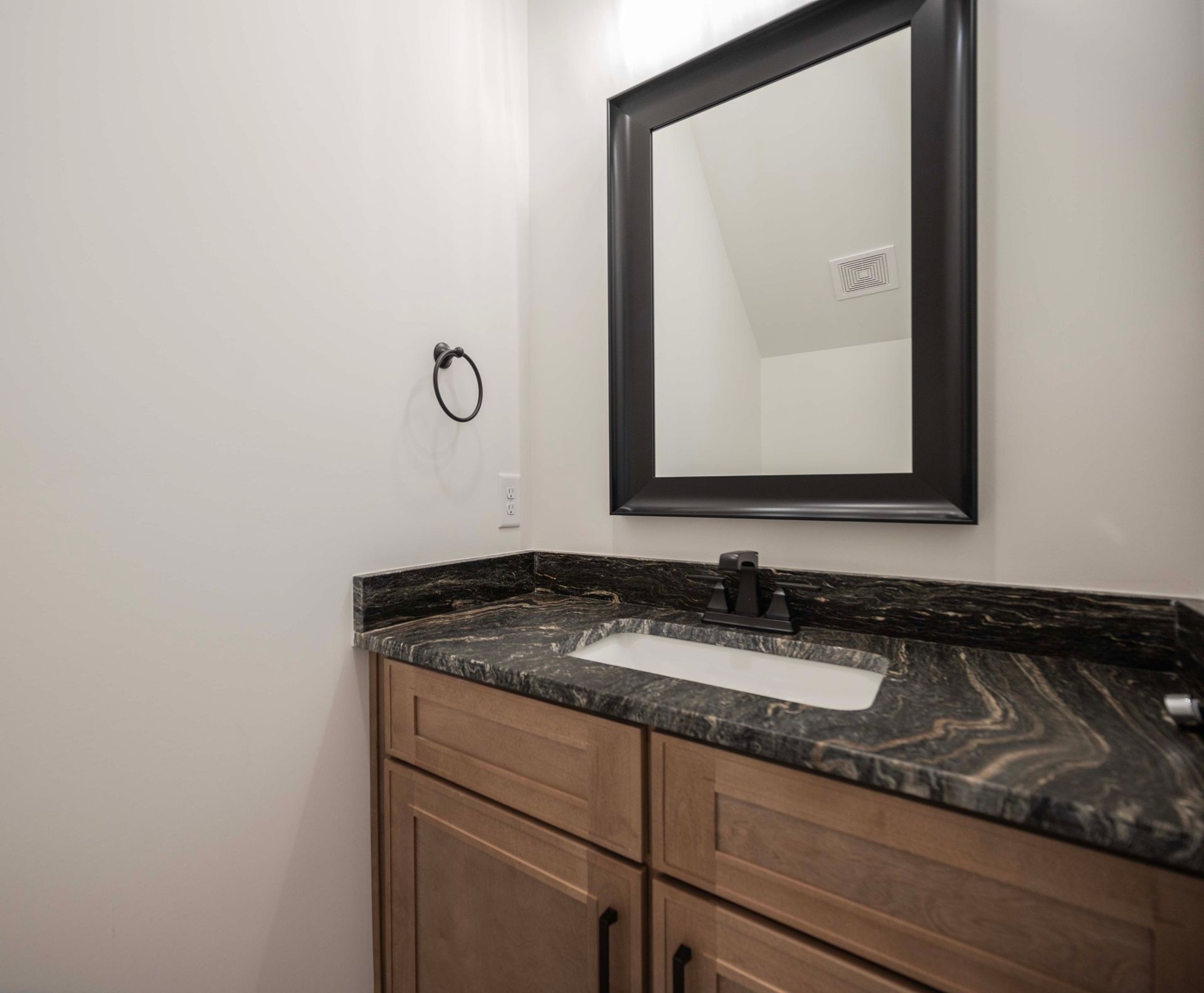 Bathroom vanity with dark granite countertop, framed mirror, and wood cabinets.