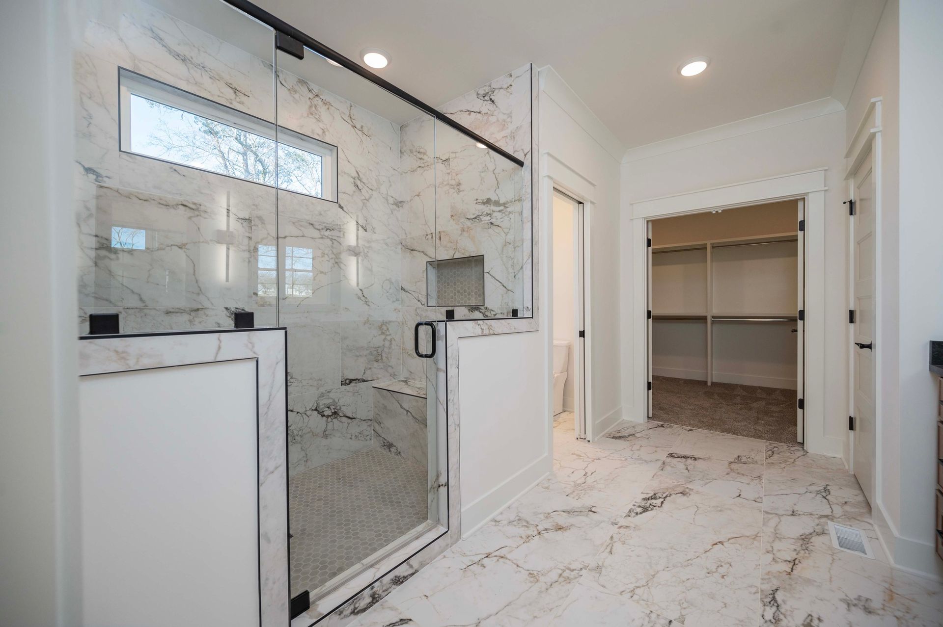 Bathroom with marble tile, a glass shower, and a walk-in closet.