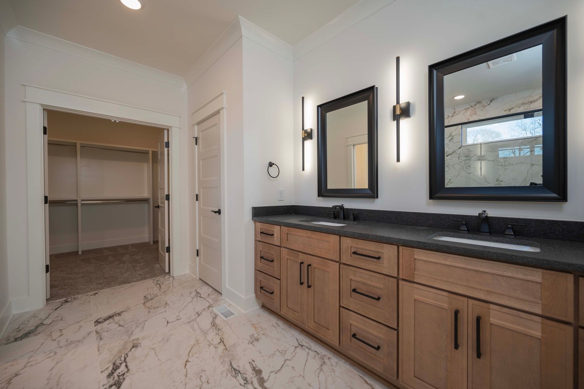 Bathroom with a double vanity, large mirrors, and a walk-in closet. Light wood cabinets and marble flooring.