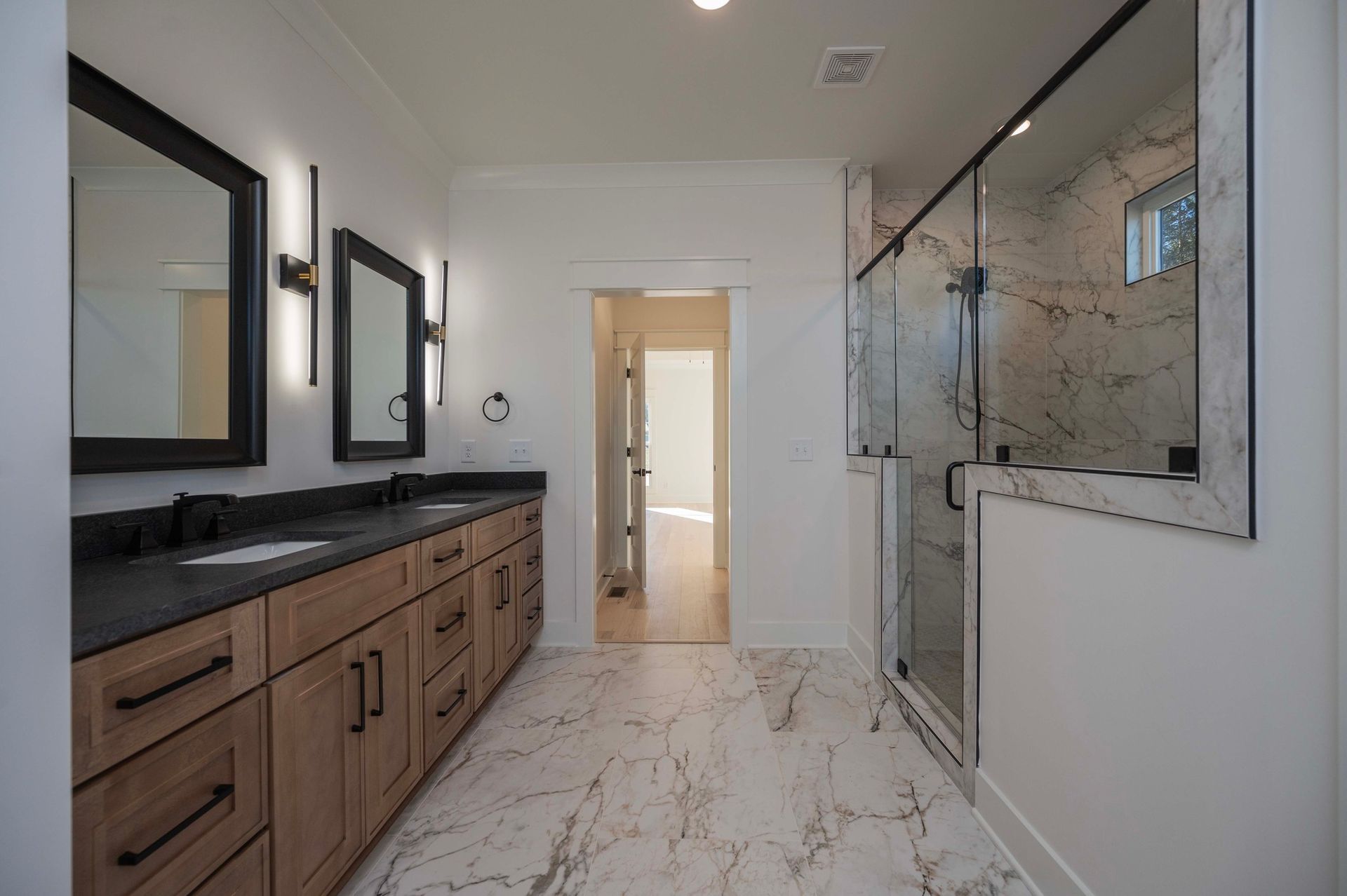 Bathroom with double vanity, marble floor, and glass shower.